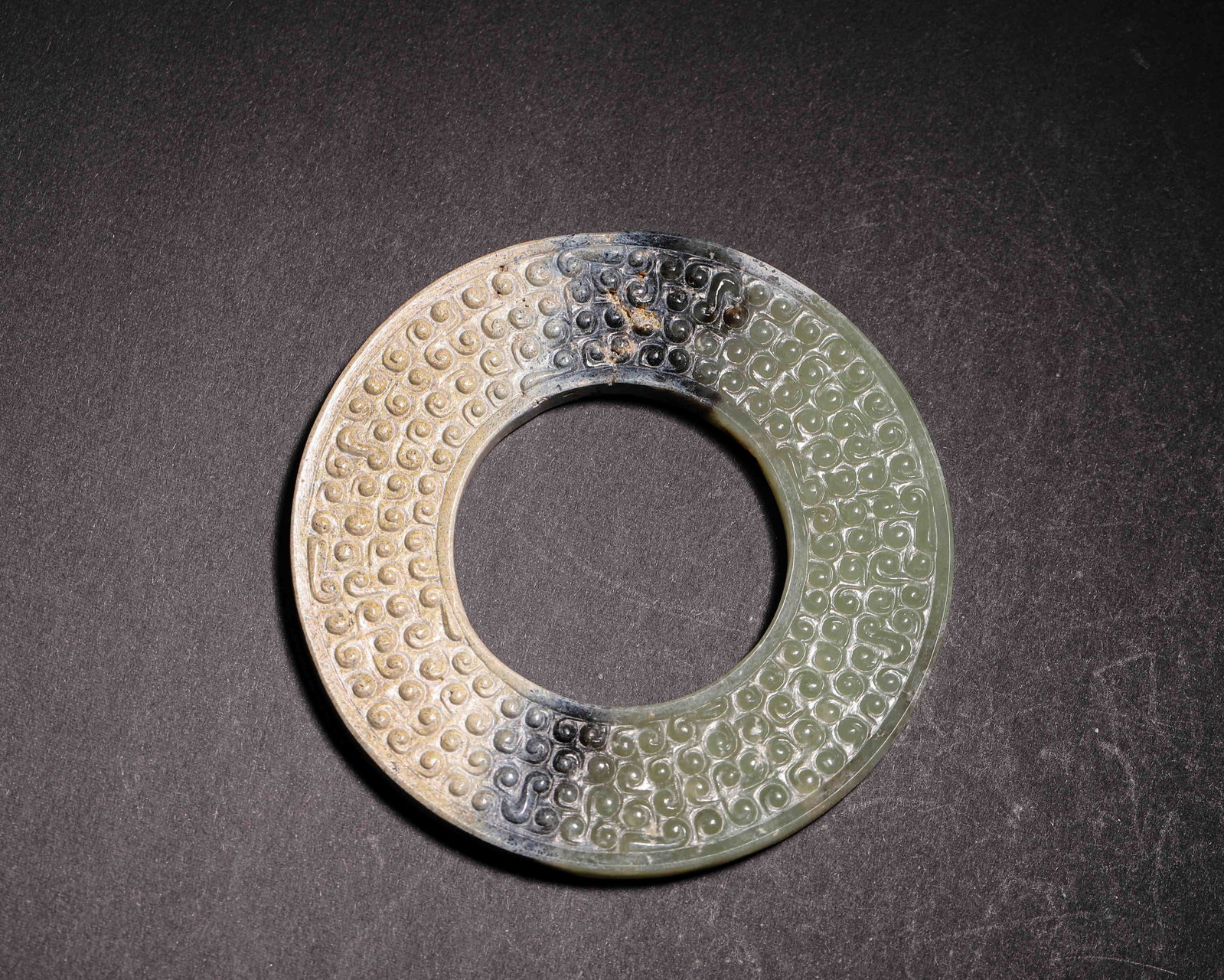 Hetian Jade Ring with Grain Pattern, Warring States Period (475-221 BC): Hetian jade ring carved with grain patterns. Partial black and earth patina, double-sided work, minor rim damage, thick patina, Warring States ritual jade. Dimensions: Diameter: 8.6cm (3.39in), Weight