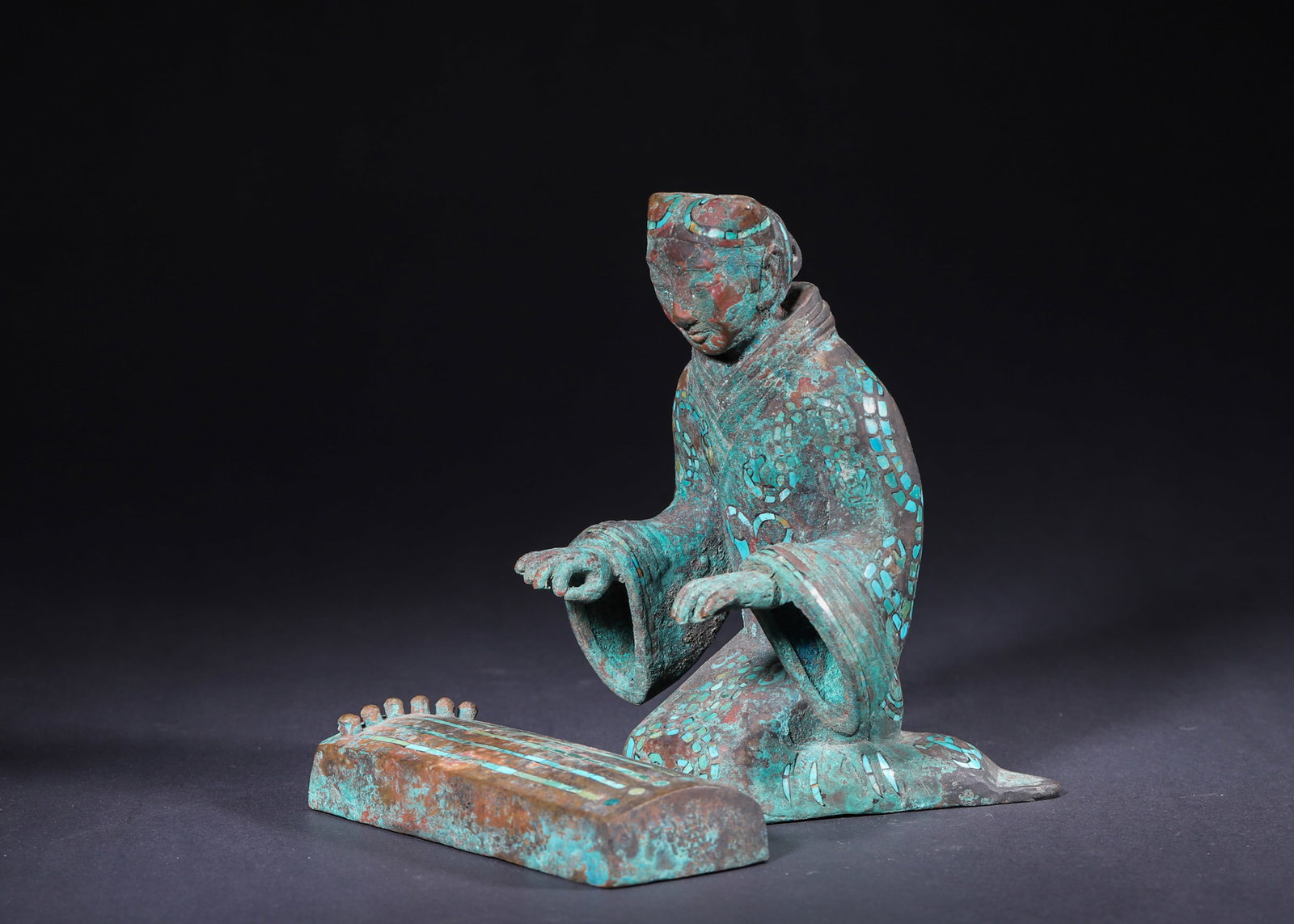 Han Dynasty, Bronze Zither-Playing Figurine with Turquoise Inlay: This Han Dynasty figurine is cast in bronze and adorned with turquoise inlay. The kneeling figure plays the zither, with phoenix motifs inlaid on its robes. It reflects the craftsmanship and musical c