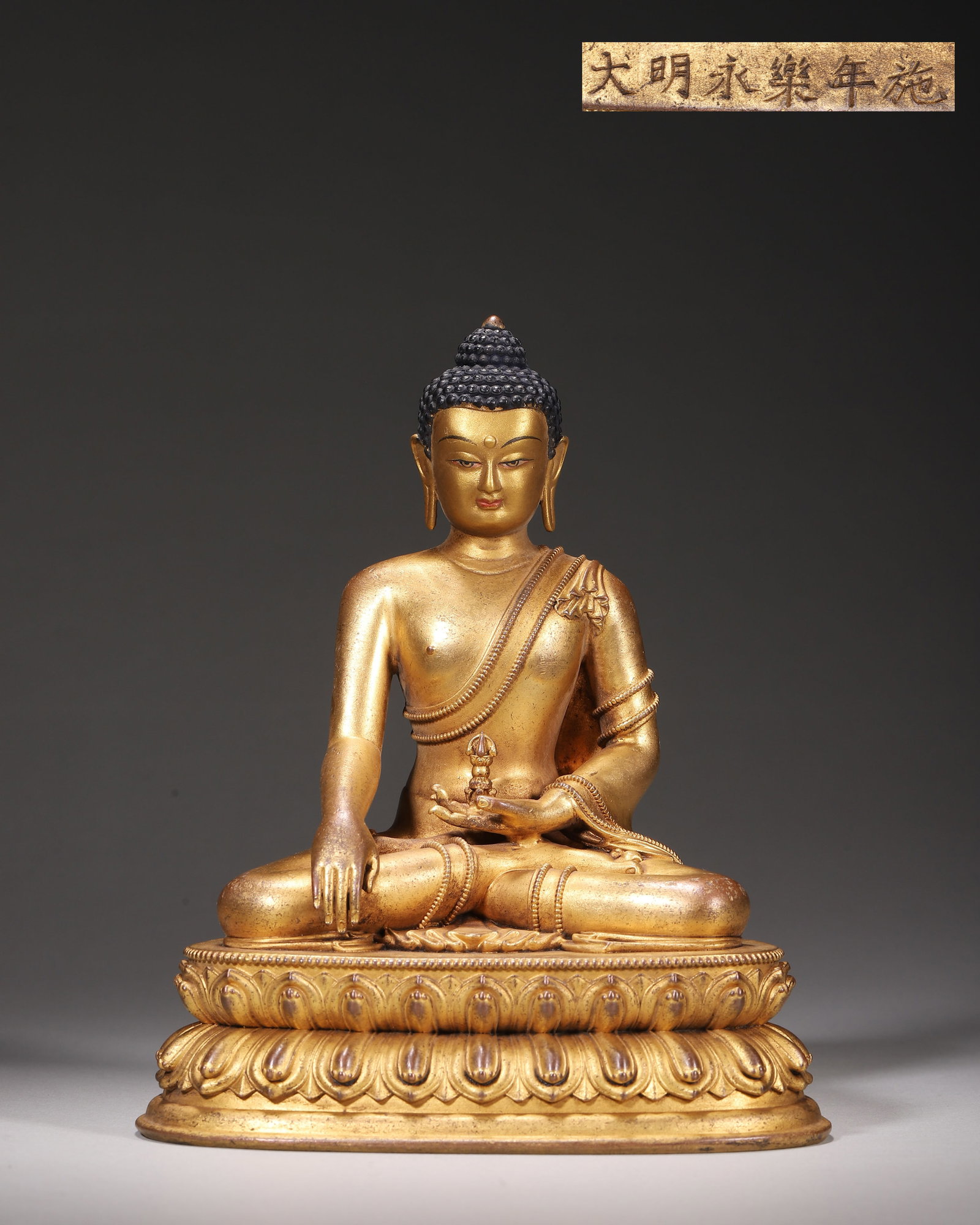 Ming Dynasty, Yongle Period (1403-1424), Gilt Bronze Seated Shakyamuni Buddha, Imperial Court Mark: Imperial court made. The Buddha sits in padmasana on double lotus base, right hand in bhumisparsha mudra, left hand holding vajra. The figure has rounded face, tightly curled hair, and a right