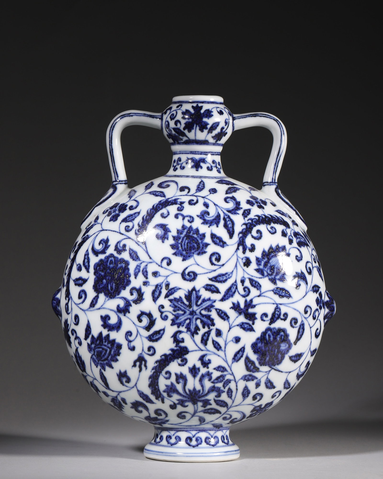 Ming Dynasty, Xuande Period, Blue and White Moon Flask with Floral Scrolls: A Ming Xuande moon flask with garlic mouth and ruyi ribbon handles, fully painted with scrolling peony, lotus and treasure flowers. Rich cobalt blue pigment with natural iron speckles, creamy white