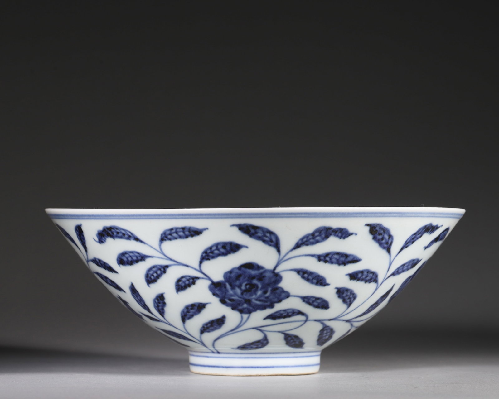 Ming Dynasty, Blue and White Conical Bowl with Interlocking Peonies, Xuande Period: Ming Xuande conical bowl with wide flared rim and narrow foot. Exterior fully painted with scrolling peony blooms in deep cobalt blue marked with natural iron specks. Double blue line borders