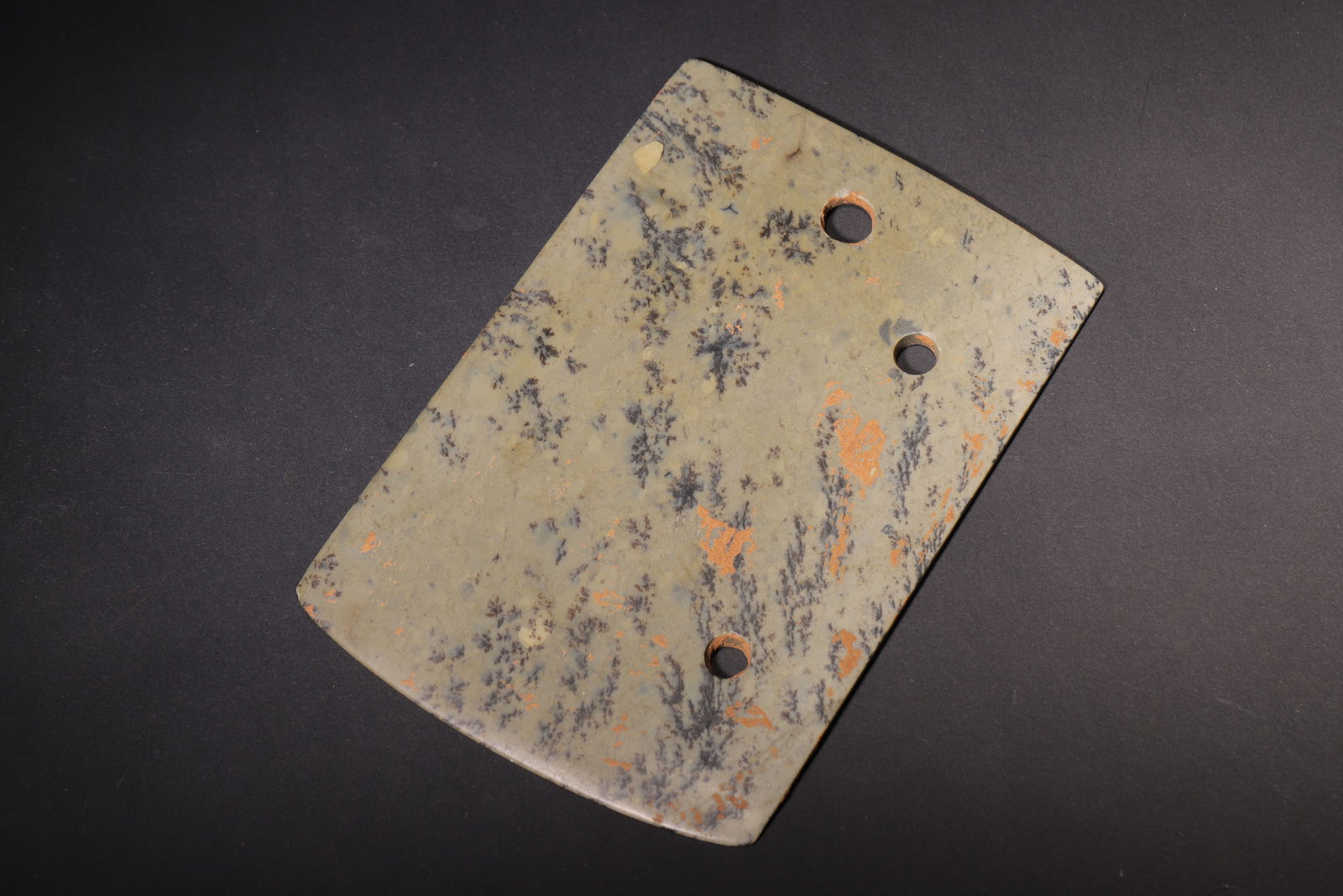 Three-Hole Jade Yue Axe, Shang Dynasty (C.1600-1046 BC): Carved from green jade naturally mottled with dendritic inclusions and orange-red soil stains. Trapezoidal flat yue form with wide curved blade, three circular perforations along the upper edge for bi