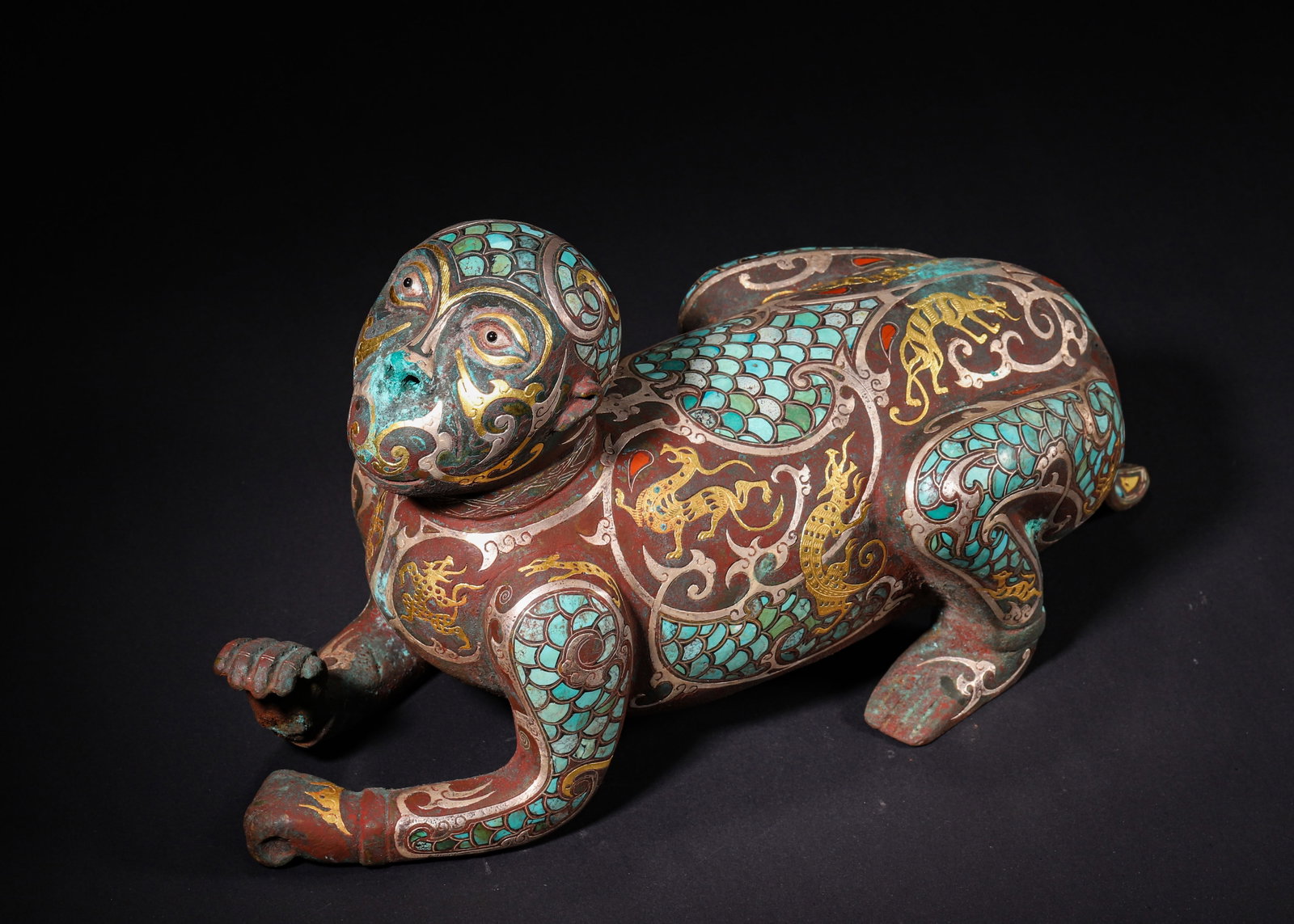 Warring States Period, Gold, Silver, and Turquoise Inlaid Bronze Monkey Weight: Cast bronze recumbent monkey weight, richly decorated with gold and silver inlay together with extensive turquoise inlay. Segmented panels bear inlaid dragon and phoenix motifs, with scale patterns