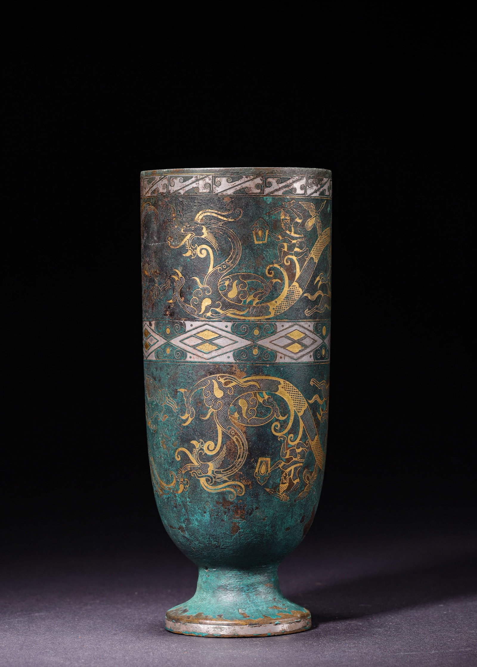 Han Dynasty, Gold and Silver Inlaid Bronze Stemmed Cup with Dragon and Phoenix: Straight cylindrical bronze stemmed cup supported by a circular foot. The vessel adopts gold and silver inlay technique, decorated all over with dragons, phoenixes and auspicious beasts separated by