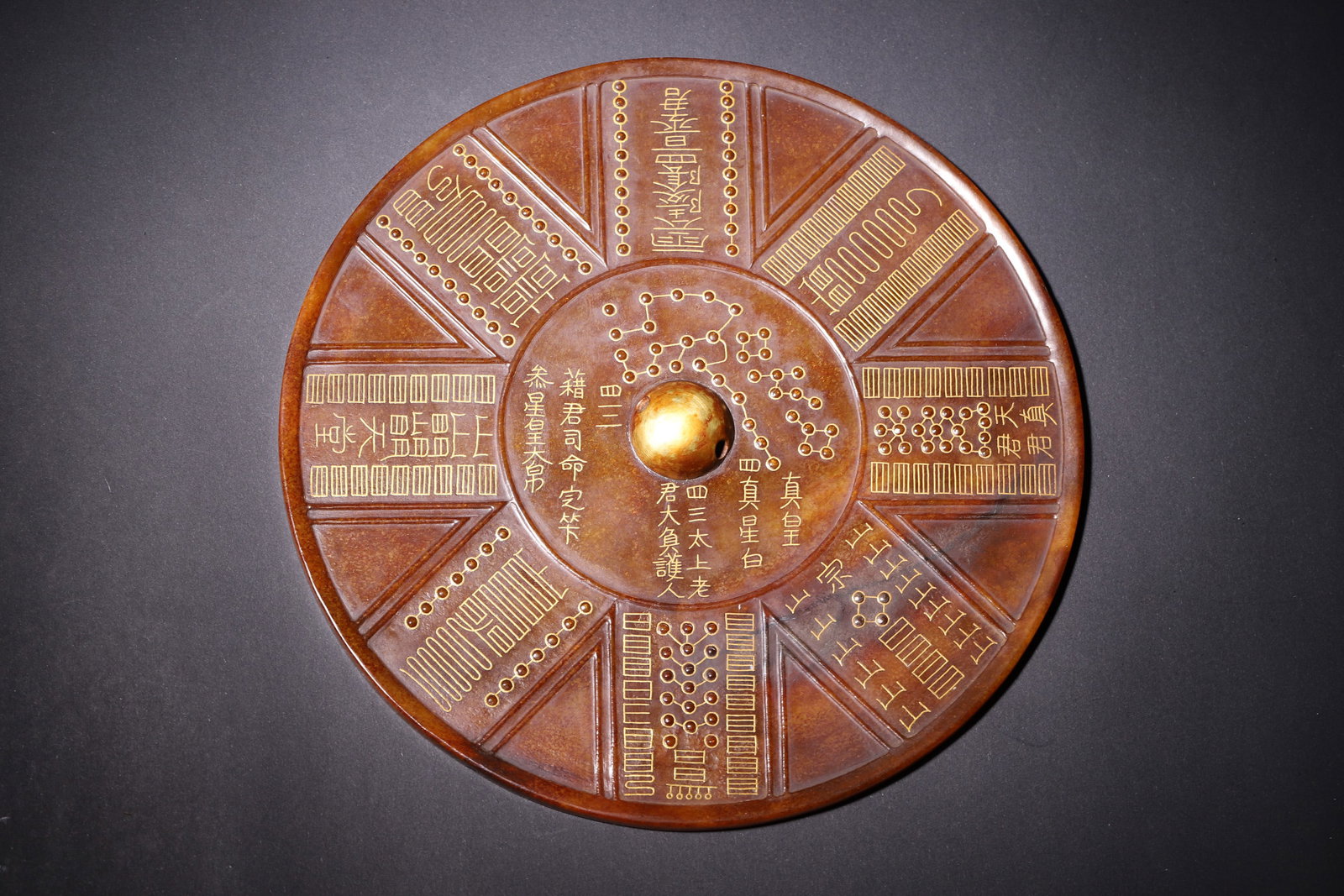 A Taoist Astrological Gold-Painted Jade Mirror-Tang Dynasty: This jade mirror is crafted from ancient jade with a deep brown patina and rich aged coating. It features a gilded knob at the center, adorned with gold-painted Big Dipper constellations, Taoist talis
