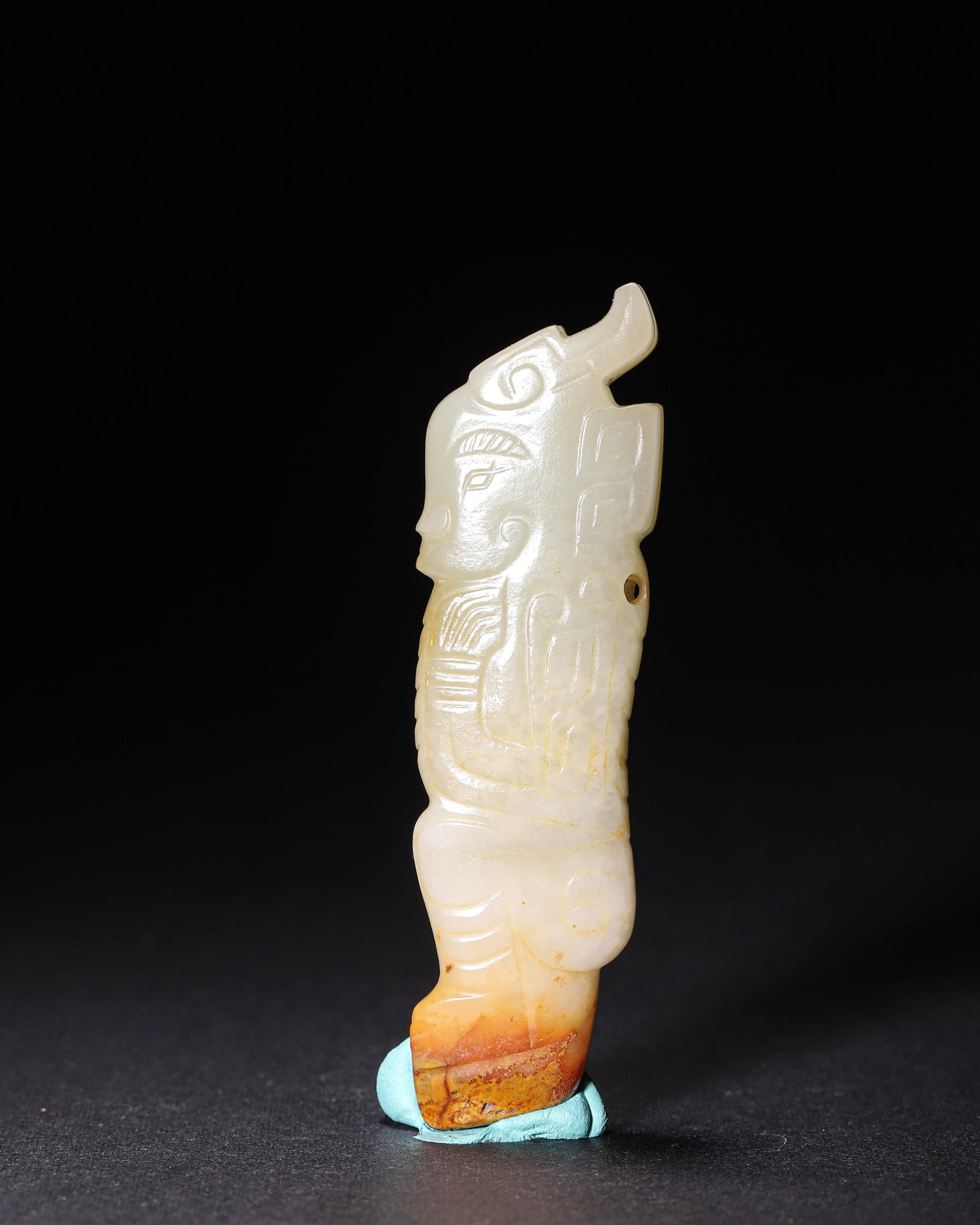 Jade Deity-Figure Pendant, Shang Dynasty (1600-1046 BC): Hetian white jade carved with typical Shang-style incised deity patterns. The lower part shows reddish-brown patina.A suspension hole on side. Neat polish and natural patina. Dimensions: Width: 2cm (0