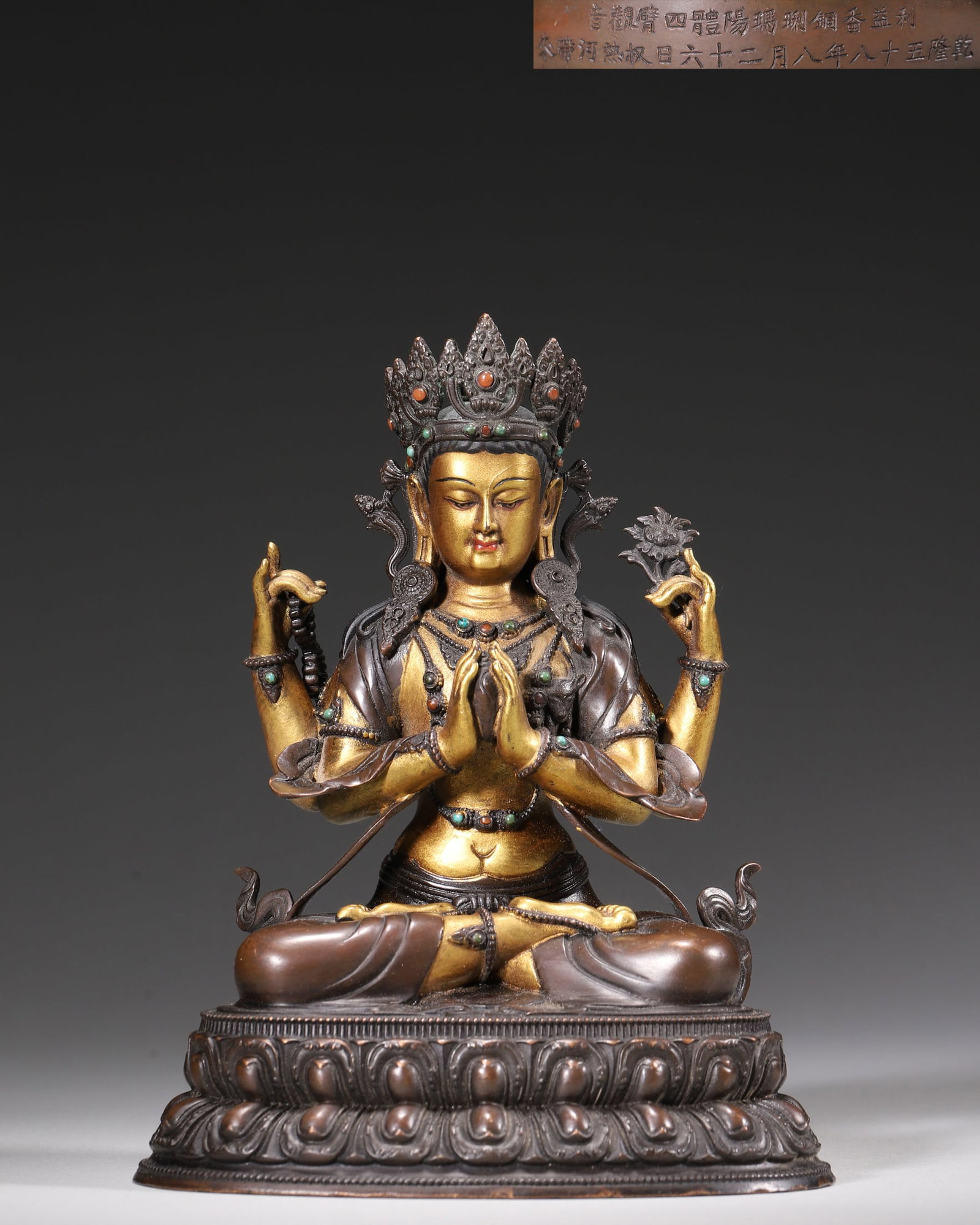 Qing Dynasty, Palace-Made Partially Gilt Bronze Statue of Four-Armed Guanyin, Qianlong Period: A palace-made partially gilt bronze statue of Four-Armed Guanyin from the Qianlong period. The deity sits on a lotus throne with a compassionate expression. The statue bears a dated inscription, indic