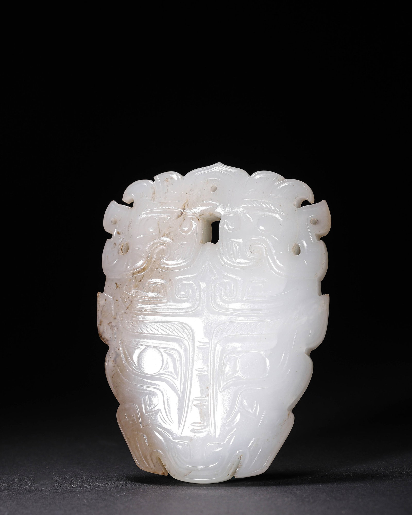 Hetian Jade Pendant with Beast-Mask and Double-Dragon Motifs, Zhou Dynasty (1046 BC-256 BC): Hetian white jade with partial dark-brown suffusion. Pendant shaped, double-dragons carved atop beast-mask, multiple openwork holes, neat incised lines and mild patina, a Zhou jade ornament. Dimension