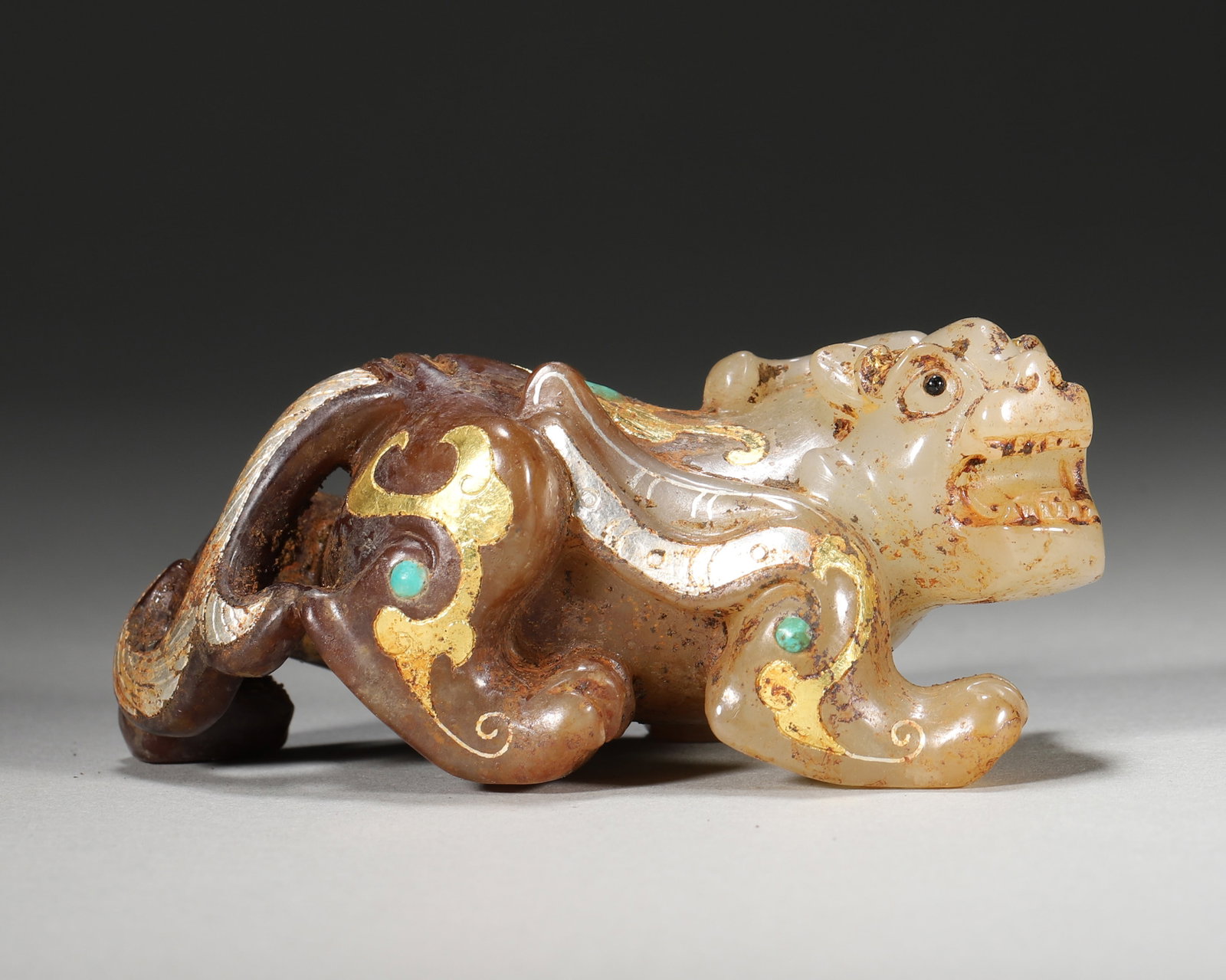 Han Dynasty Hetian Jade Gold and Silver Inlaid Turquoise Mythical Beast Ornament: Patinated jade; carved into a coiled dragon huang beast, decorated with Cuo Jin silver cloud patterns & turquoise accents. Follows Warring States Han Cuo Jin silver jade techniques. A fusion masterpie