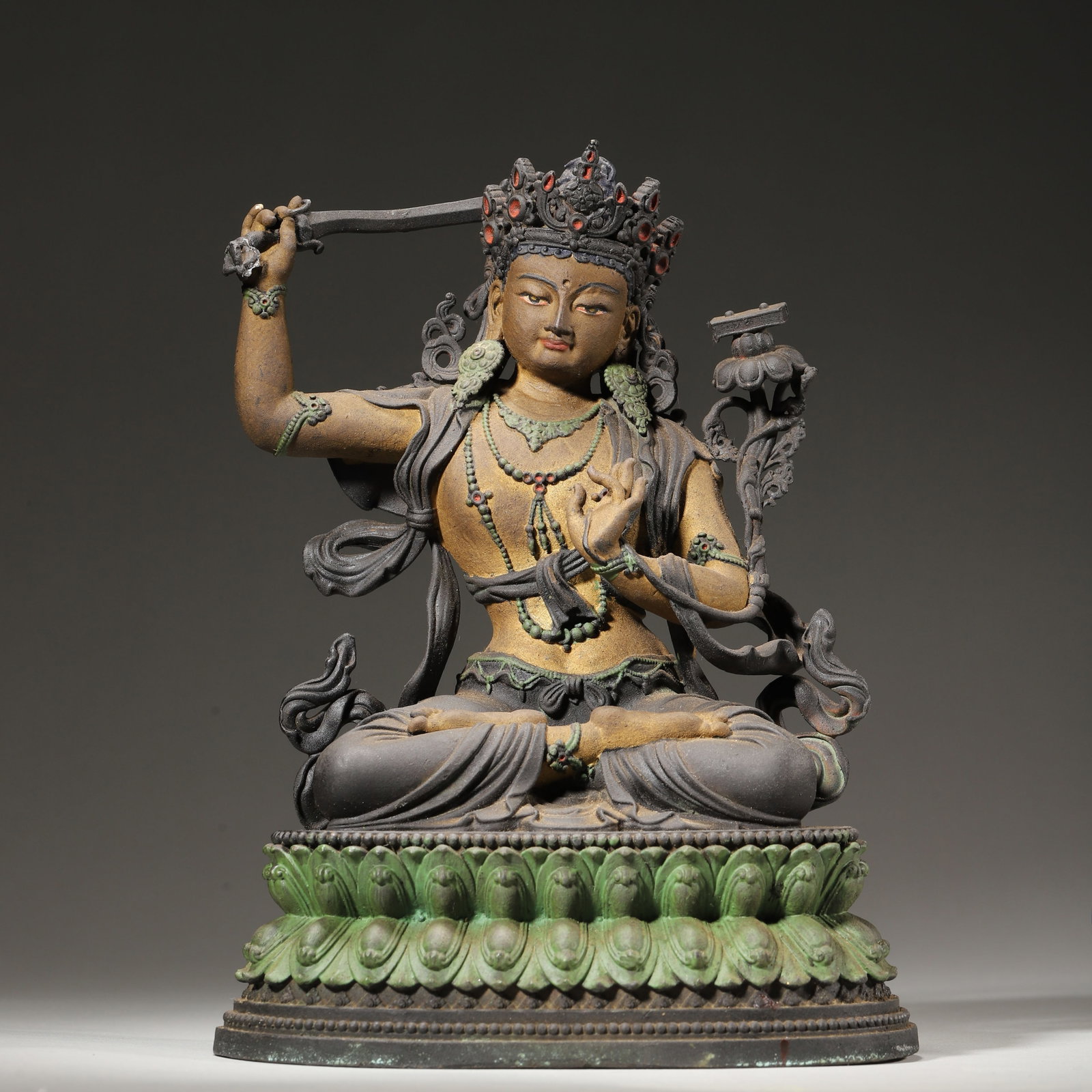 Qing Dynasty, Painted Bronze Seated Statue of Manjushri Bodhisattva: Cast bronze figure polychromed with mineral pigments. Manjushri sits in full lotus posture on double lotus base, wielding the sword of wisdom in right hand, left hand holding a lotus stem surmounted b
