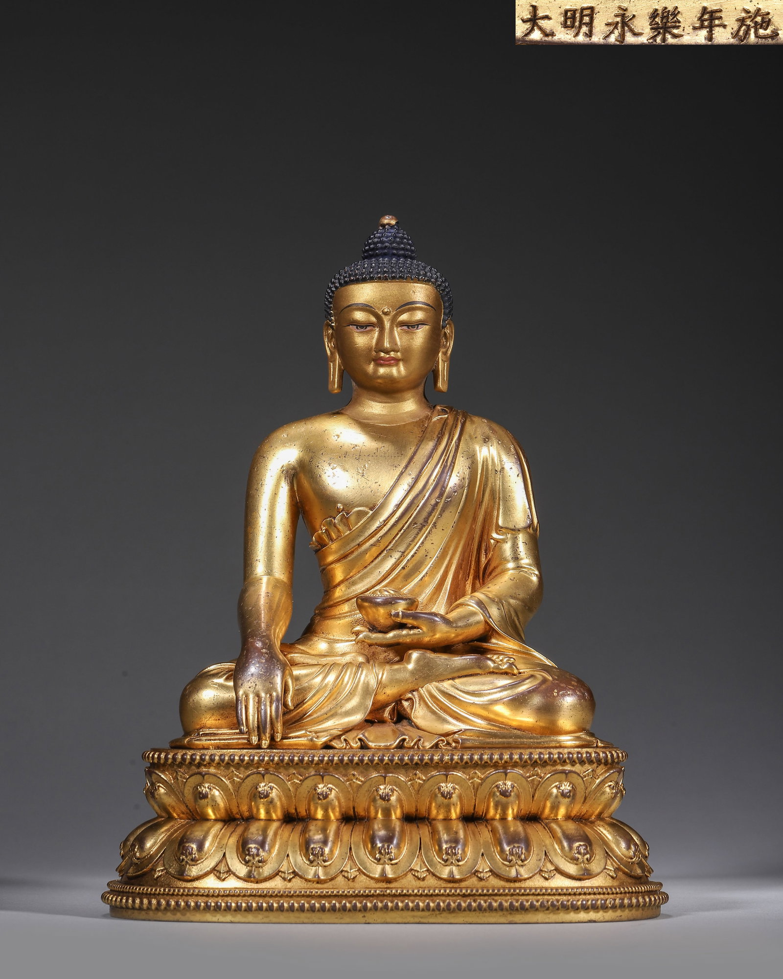 Imperial Gilt-Bronze Seated Sakyamuni Buddha, Ming Yongle Period, 1403-1424: Buddha seated in full lotus on double lotus throne,right hand in earth-touching gesture,left hand holding alms bowl. Inscribed "Bestowed in Yongle Reign",a fine Ming imperial statue. Dimensions: Lengt