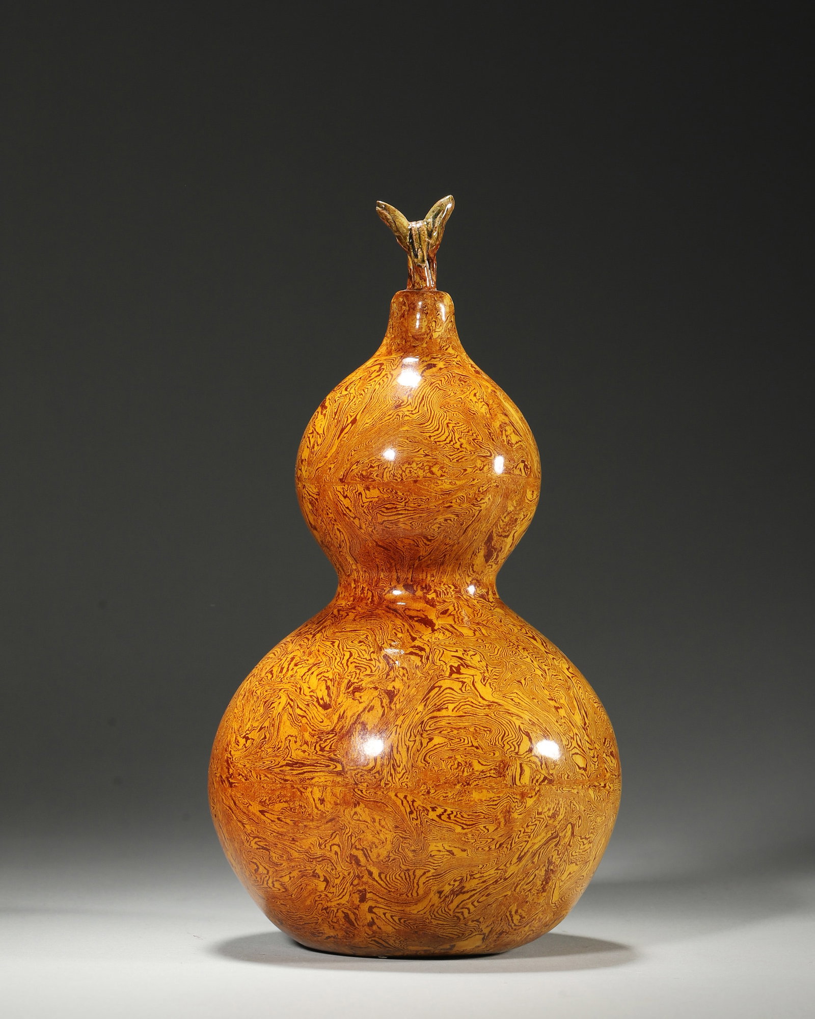 Marbled Glaze Gourd-Shaped Vase, Tang Dynasty, 618-907: Double-gourd form with stem-leaf finial. Covered with marbled glaze of interwoven yellow-brown veins, glossy surface. Hole on base, well-proportioned shape. Dimensions: Diameter: 11cm (4.33in), Height