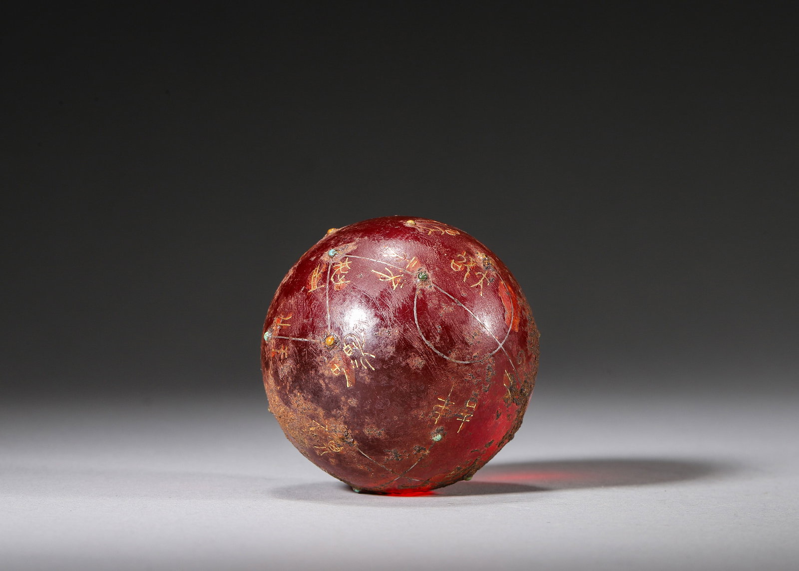 Gold Inlaid Turquoise-Set Red Glass Celestial Sphere, Han Dynasty (202 BC-220 AD): Polished monolithic translucent wine-red glass sphere covered in ancient burial patina and encrustation. Silver lines trace celestial orbits, fine gold inlay bears archaic star nomenclature characters