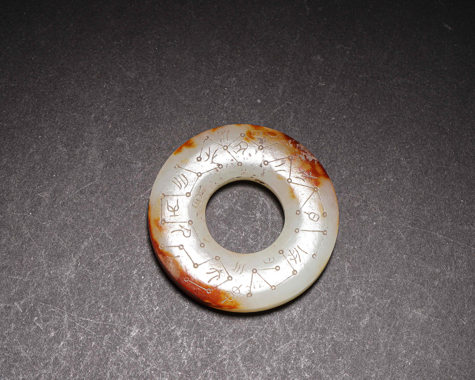 Han Dynasty (202 BCE 220 CE), Hetian Jade Ring with Incised Astronomical Inscriptions: Carved from Hetian jade with reddish brown inclusions. Flat annular form, both sides incised with star maps and archaic characters. Mellow patina, well preserved. Dimensions: Diameter: 5.6cm (2.2in), 