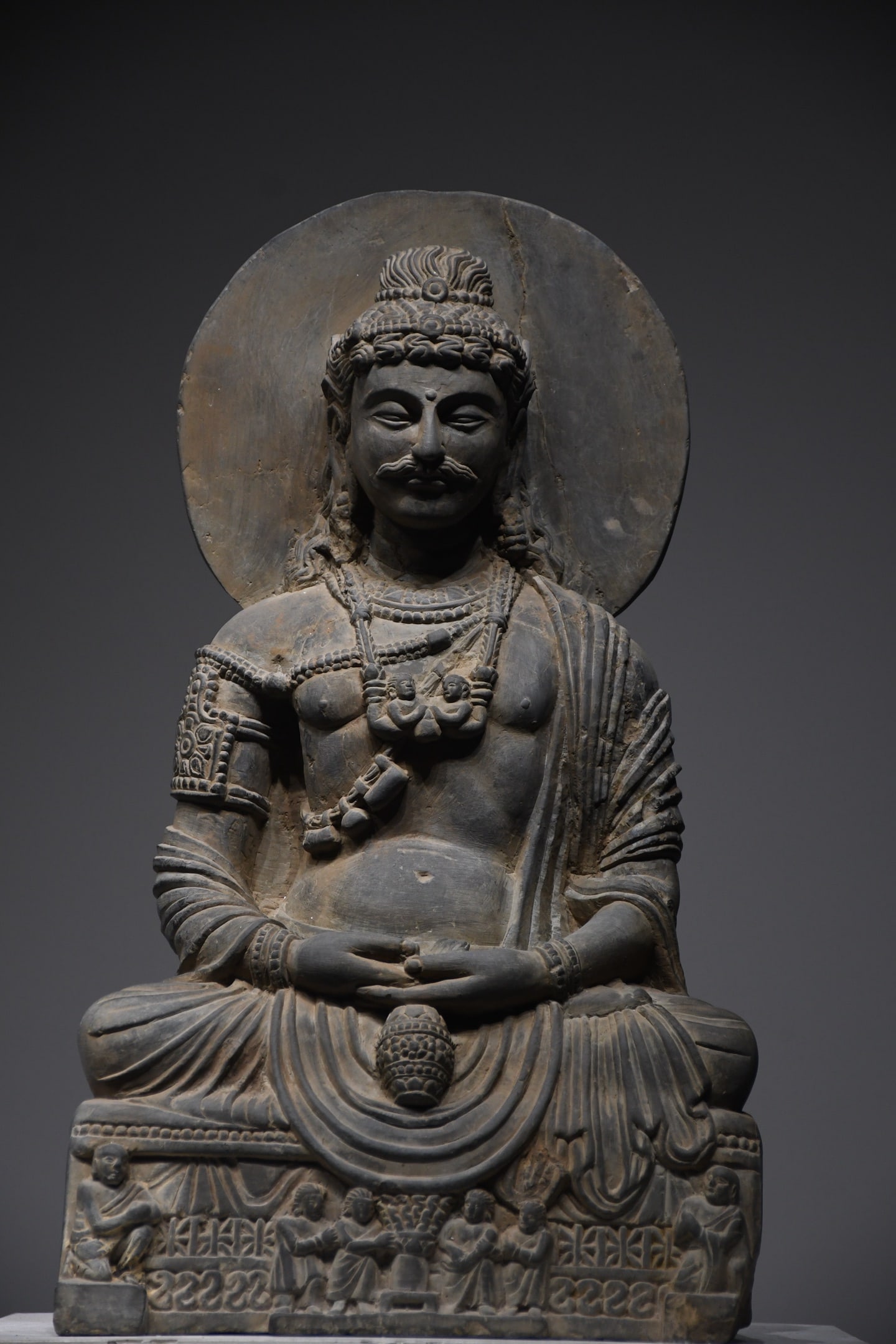 A Gandhara Style Stone Seated Maitreya Bodhisattva, Kushan Dynasty, 2nd-3rd Century: Gray schist stone carved Maitreya Bodhisattva statue in Gandhara style, Kushan Dynasty, 2nd-3rd century. The Bodhisattva sits in dhyana mudra holding a lotus bud, with curly crown and plain halo, clas