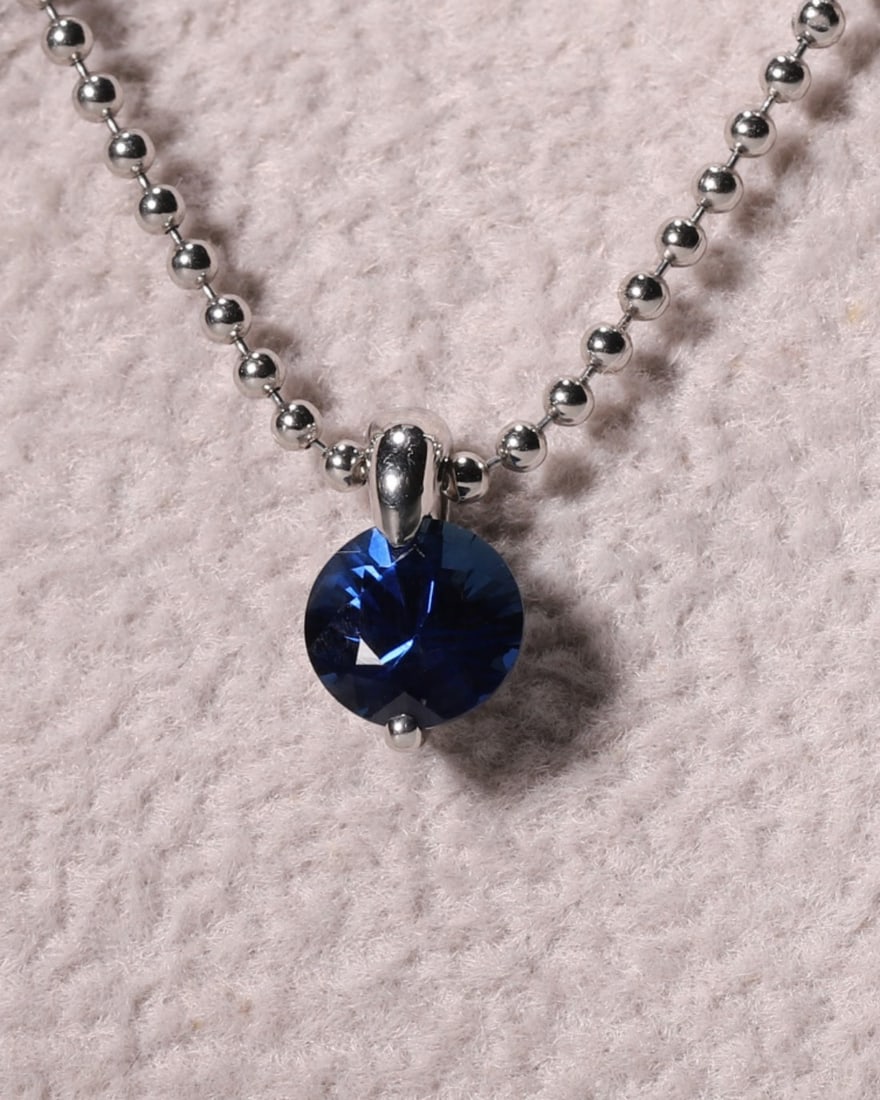 An 18K White Gold Solitaire Round-Cut Sapphire Pendant Necklace: Vertical Drop Set with single round brilliant-cut royal-blue sapphire in minimal two-prong 18K white gold setting, paired with fine ball chain. Sleek minimalist design suits daily wear and fine gemsto
