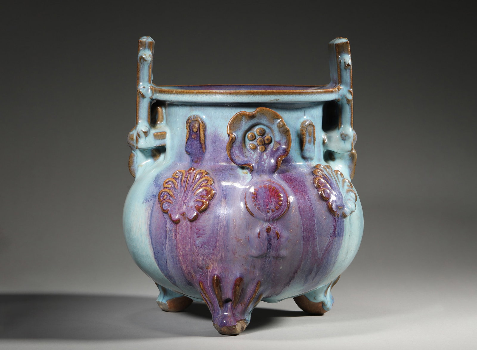 Jun Yao Flambe-Glazed Tripod Censer with Dragon Appliqué, Yuan Dynasty, 1271-1368: Tripod censer with upright handles and beast-form feet. Appliqué dragon and floral motifs. Glaze blends blue and purple hues. Unglazed base reveals coarse ceramic body. Dimensions: Diameter: 22cm (8.