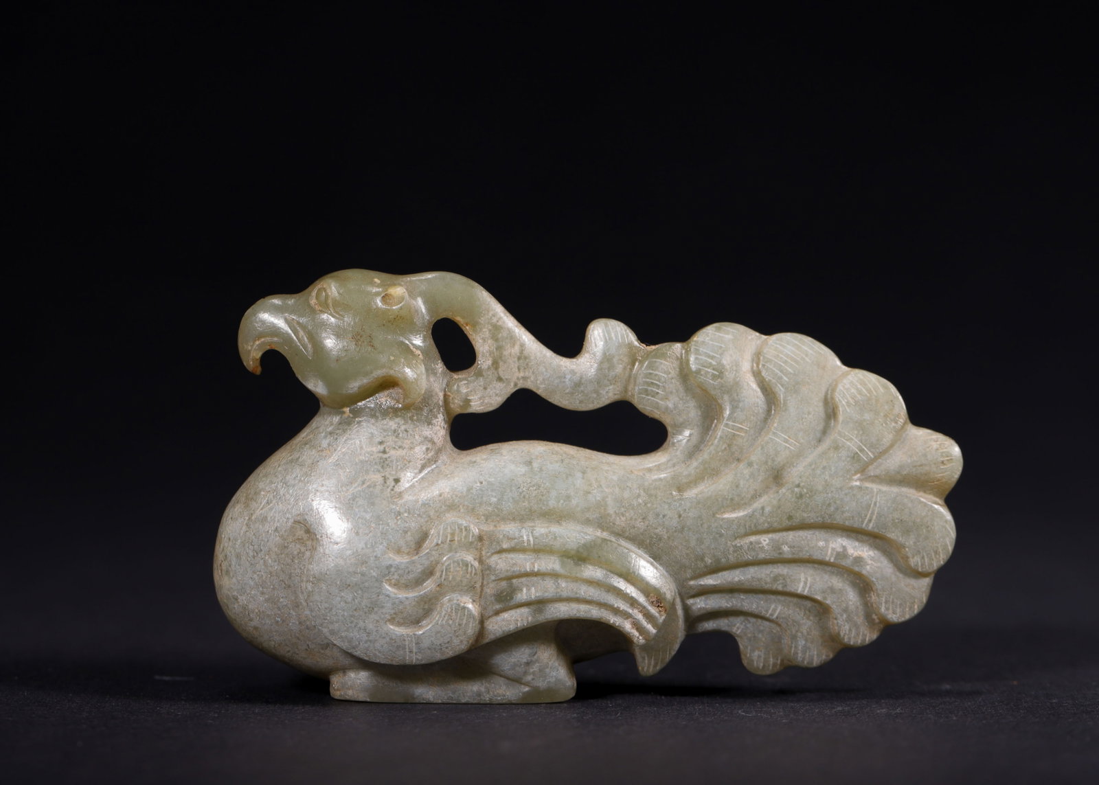 Celadon White Jade Phoenix Pendant, Han Dynasty (202 BC-220 AD): Carved from celadon white jade suffused with pale grayish-white calcified patina. Fully modeled recumbent phoenix with sharp beak and rounded eyes. Openwork scroll ribbon rises behind its neck; incise