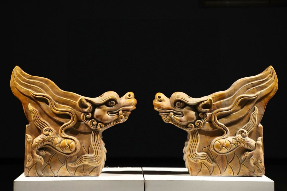 Ming Dynasty, A Pair of Yellow-Glazed Pottery Roof Figures of Dragon-Headed Beasts: This pair of yellow-glazed pottery roof figures, from the Ming Dynasty, is crafted from red pottery with a lustrous yellow glaze. The dragon heads are raised, with flowing manes and swirling cloud mot