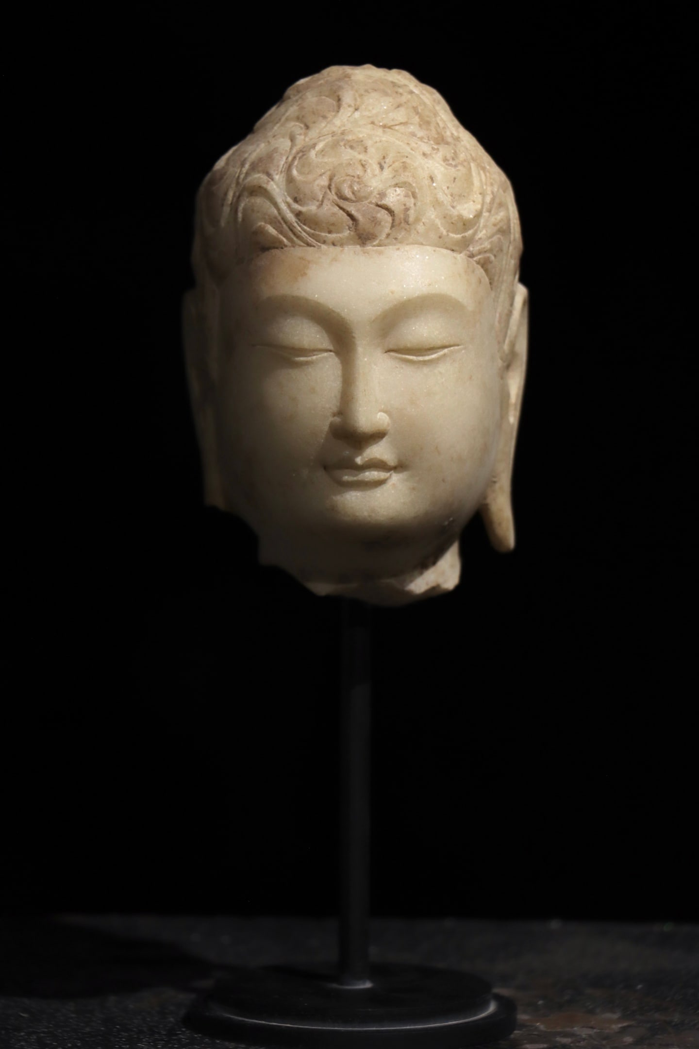 White Marble Head of Buddha, Tang Dynasty (618-907 AD): Head of Buddha carved from fine white marble with smooth and pale texture. The hair is sculpted in fluid whorled curls with distinct layered lines. The face is plump and gentle, eyes lowered peacefull