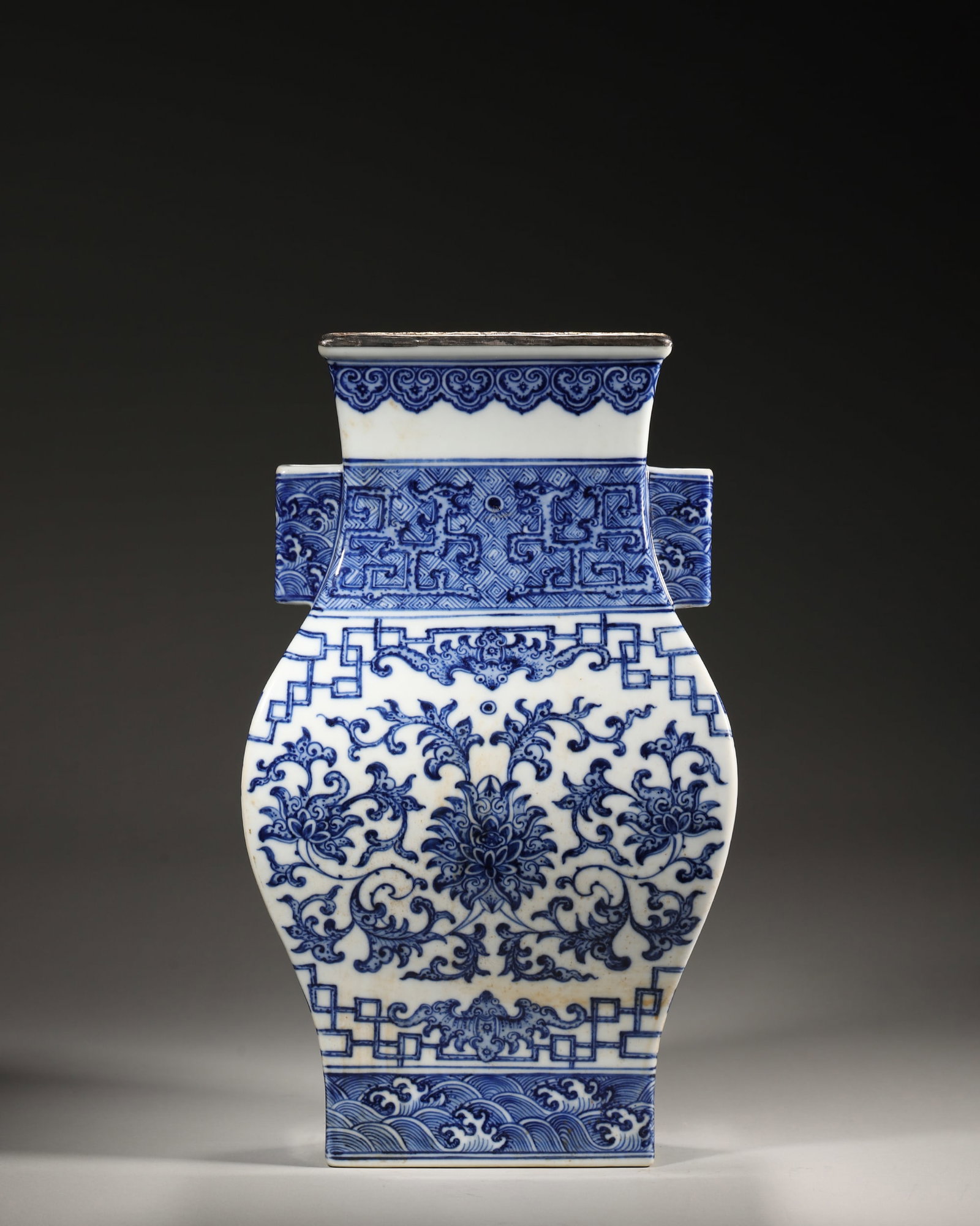 Blue and White Square Vase with Handles and Intertwined Lotus (Yongzheng, Qing, 1723-1735): Square form with tubular handles and silver-mounted rim. Painted with intertwined lotus, dragon, bat and wave patterns. Distinct layered design, bright blue tone, reign mark on base. Dimensions: Lengt