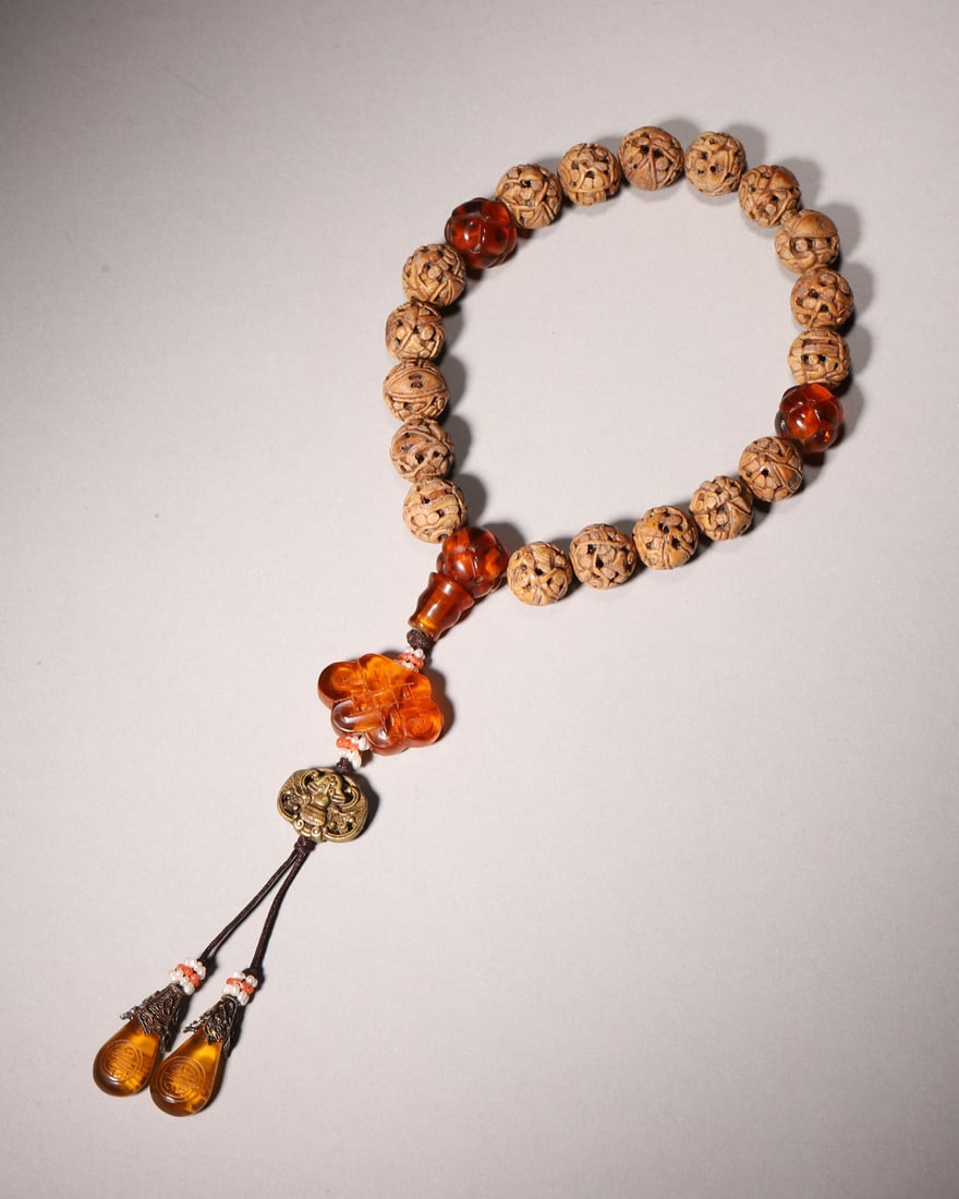 An Openwork Figure-Carved Nut 18-Bead Hand String with Glass Ornaments: This antique 18-bead hand string has hollow-carved nut beads engraved with tiny figures. It is decorated with carved glass spacers, Buddha head and Chinese-knot glass pendant, matched with bronze bles