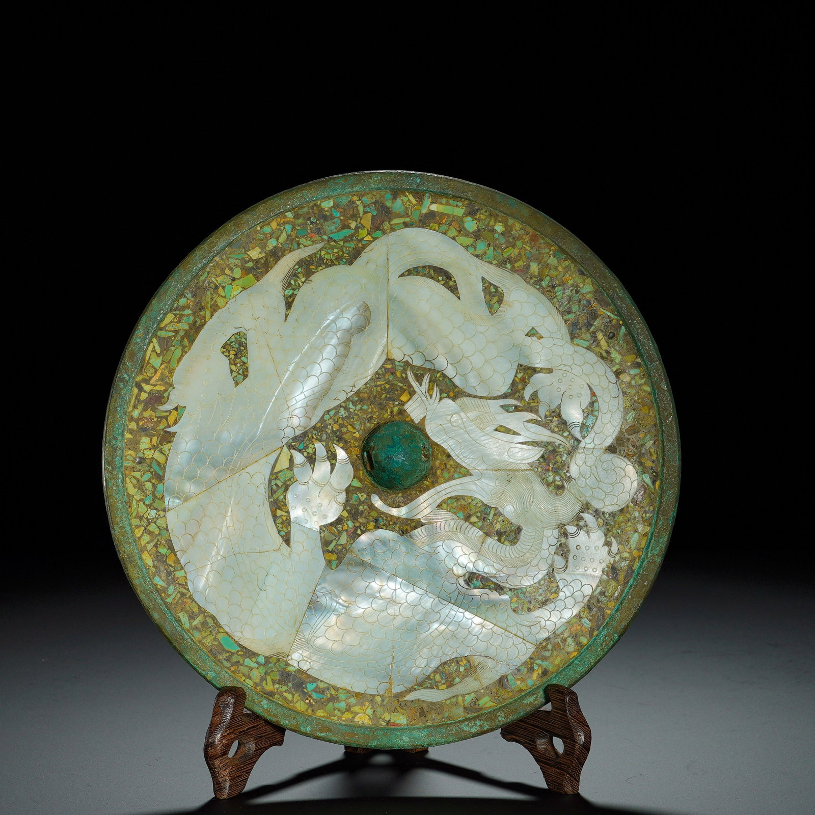 Bronze Mirrors Inlaid with Mother-Of-Pearl and Dragon Patterns: The circular Han-dynasty bronze mirror is fitted with a turquoise knob. Its reverse side is dominated by a coiled flying dragon motif meticulously inlaid with mother-of-pearl, with clearly rendered sc