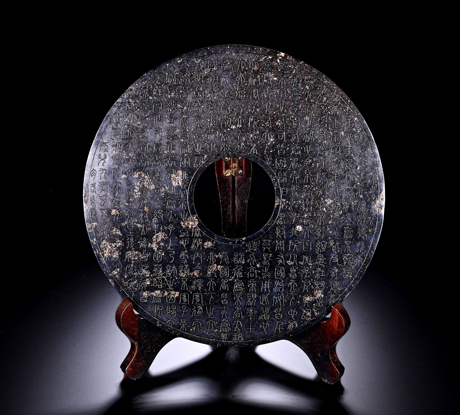 Han Dynasty, Black Jade Disc with Inscriptions All Over: This standard circular ritual bi disc is carved from deep black jade, with central aperture. The surface is covered with mottled burial encrustation and profound aged patina. Dense ancient seal-script
