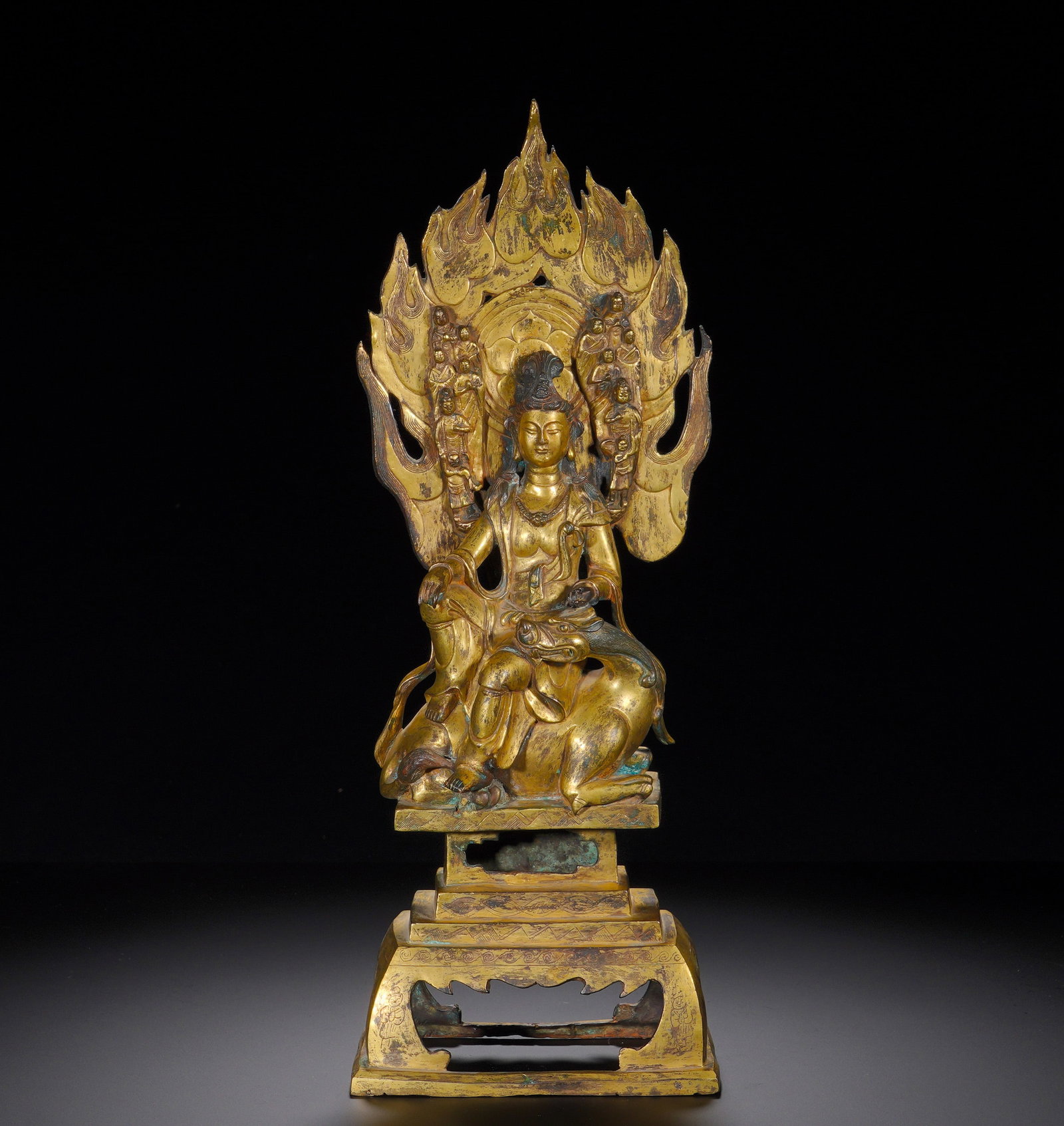 Tang Dynasty, Gilded Bronze Hou-Beast Statue of Guanyin: Cast bronze with gilding. The Bodhisattva sits in relaxed posture upon a mythical hou beast, with serene, merciful facial features, elaborate headdress, necklaces and flowing robes. A large flame mand