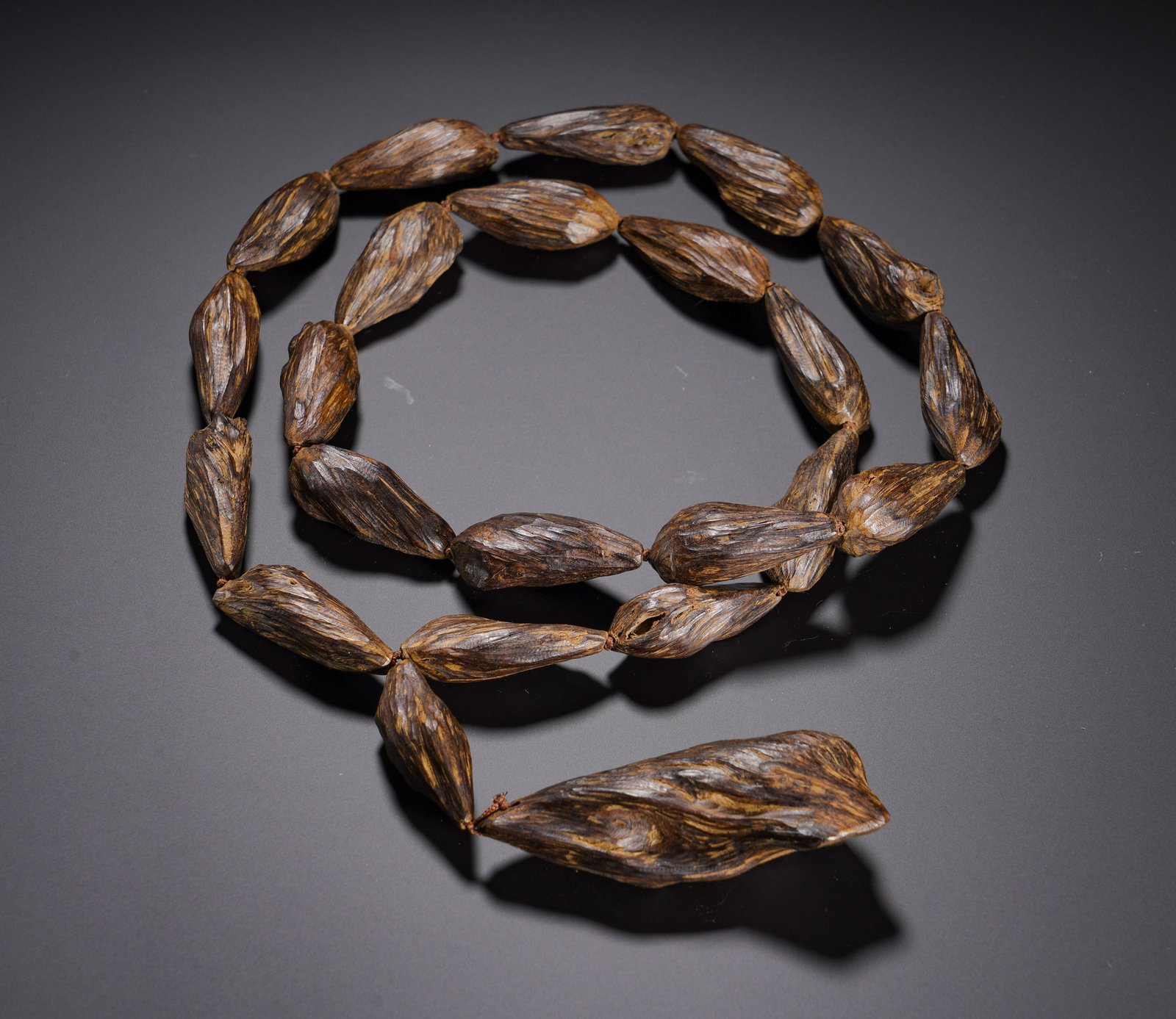 Qing Dynasty, String of Shaped Agarwood Beads: Strand of natural agarwood beads of Qing dynasty. Beads are tapered and shuttle-shaped with uneven sizes, retaining original wood texture. Dense interwoven oil streaks of dark-brown and golden-yellow 