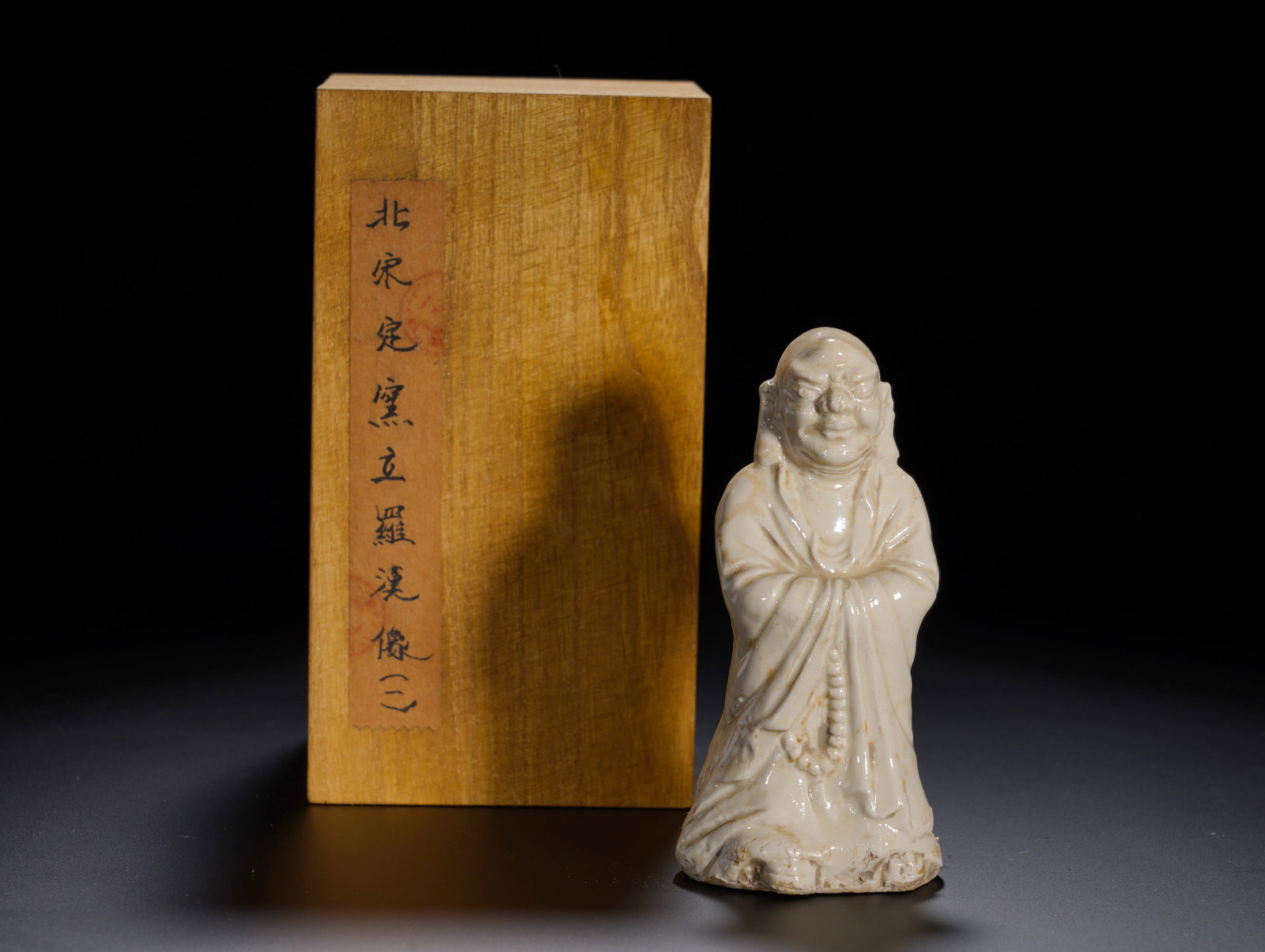 Northern Song Dynasty, White Glazed Standing Arhat from Ding Kiln: A standing Luohan figure of Northern-Song Ding-ware. The luohan stands upright with stylized, expressive facial features and large pendulous ears. Dressed in cross-collared monk??s robe with hands con