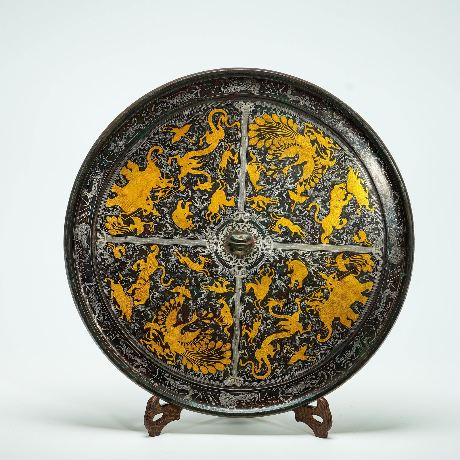 Han Dynasty, Bronze Plate with Inlaid Gold and Silver Patterns of Four Gods and Auspicious Beasts: The large Han-dynasty bronze plate has broad flared rim and raised central knob. Its surface is partitioned into four quadrants by silver-inlaid lines against silver-inlaid swirling cloud-qi backgroun