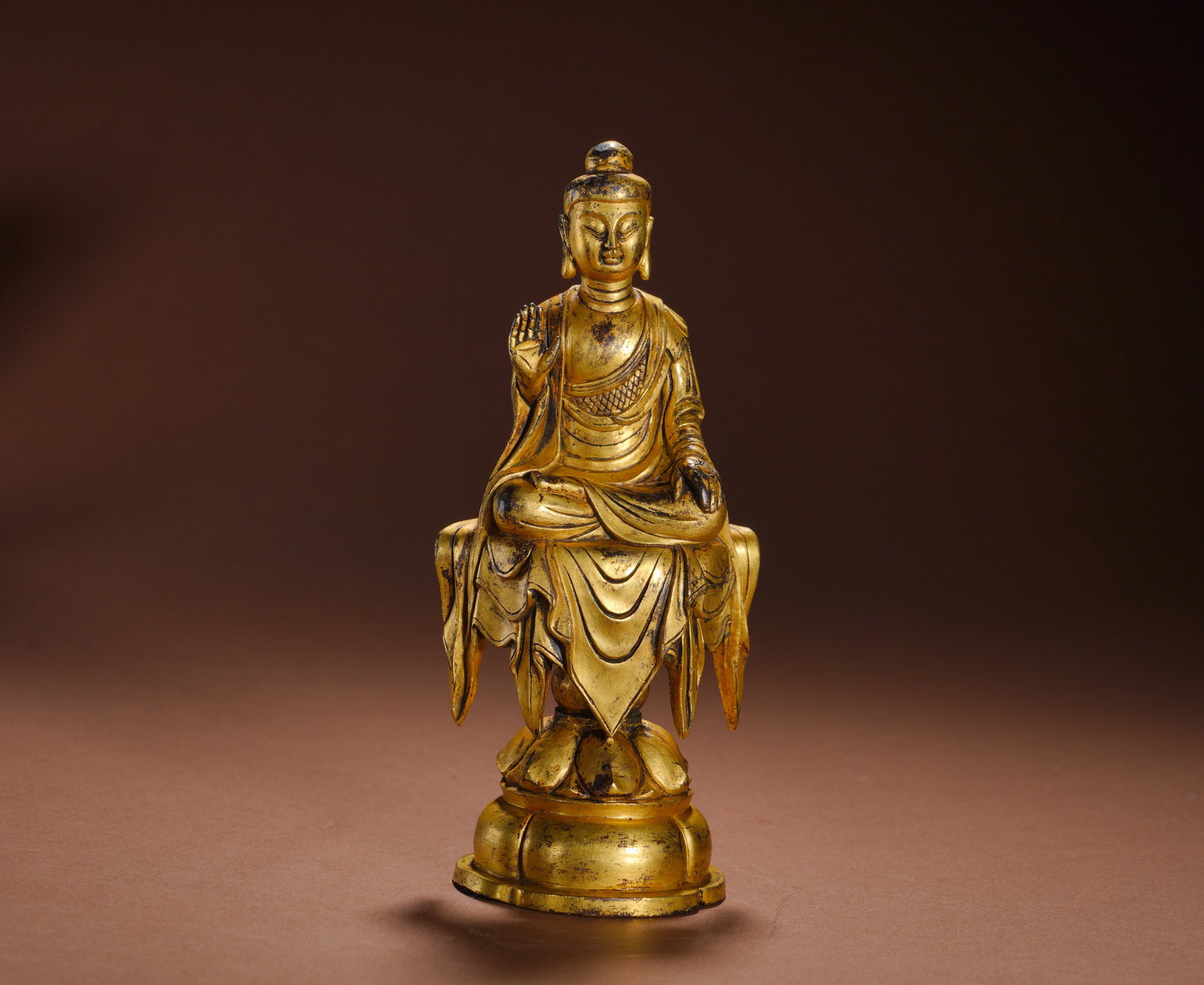 Tang Dynasty, Gilded Bronze Statue of Sakyamuni Sitting Buddha: Cast bronze with full gilding. The Buddha sits cross-legged on an upward lotus base, right hand raised in Abhaya Mudra, left hand resting on knee. With rounded ushnisha and serene facial expression, h
