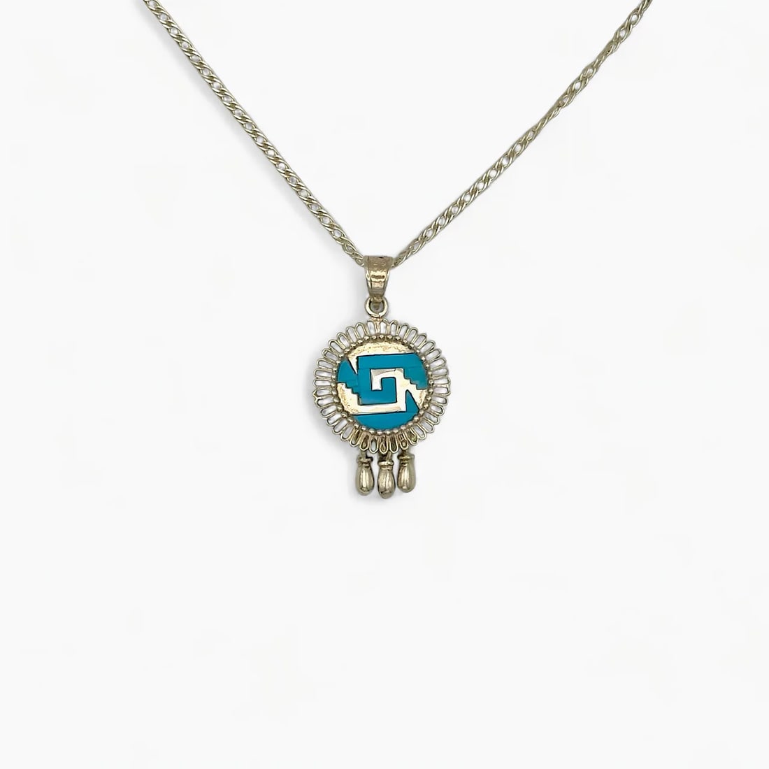 "Shield of Echoes" Turquoise Pendant: The Shield of Echoes Pendant by Oro de Monte Albán distills the power of Mesoamerican symbolism into a compact, finely crafted form. Centered on a round silver medallion with a turquoise-inlaid glyph