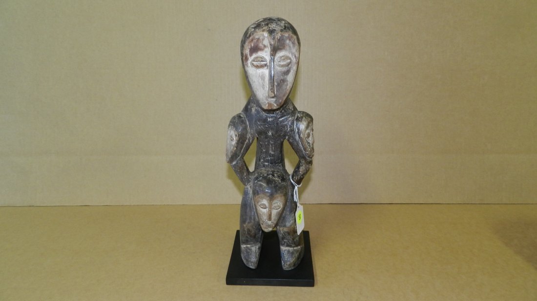 9365) African carved Lega standing figure, with: 9365) African carved Lega standing figure, with multiple maskettes on body, on display stand, COND G, 14 1/2 Tall