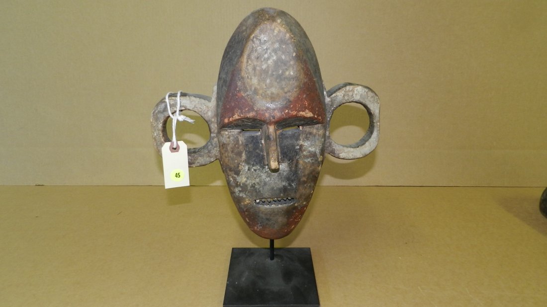 422) BOA FACE MASK. Wood with reddish brown, white and: 422) BOA FACE MASK. Wood with reddish brown, white and black pigments, inset metal teeth. COND G, surface weathered, left ear repaired, on stand. Mask is 12 x 13 1/2 x 6, w/stand 18"