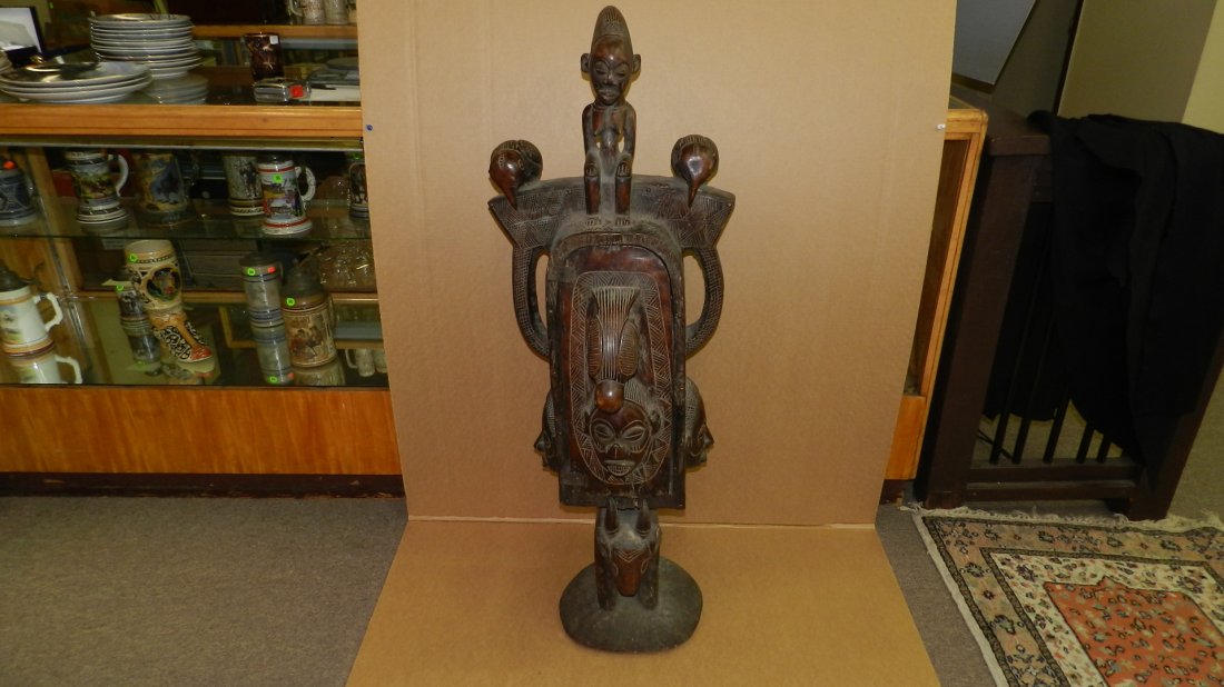 962) African carved YAKA style storage box. Wood with: 962) African carved YAKA style storage box. Wood with brown and black stains. Central cavity with large handle in form of a bird atop a human face, leather hinges. The box carried atop a small goat, s