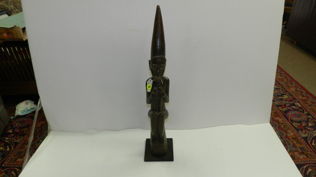 5775) African carved Seated figure with pointed hat: 5775) African carved Seated figure with pointed hat holding two staffs 22"