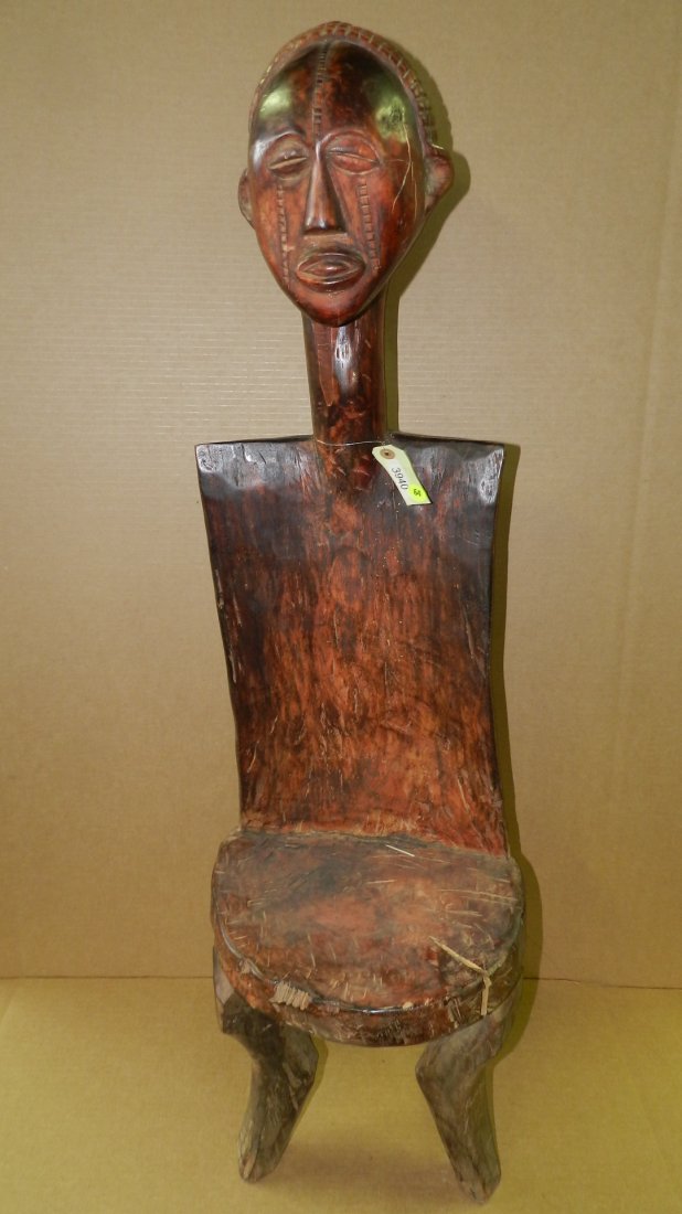 3940) East African carved chair, hardwood with: 3940) East African carved chair, hardwood with variegated orange & brown stain, rectangular back w/large human head on top. COND G, appropriate for age, origin & mediums. Single crack on base. From Ta