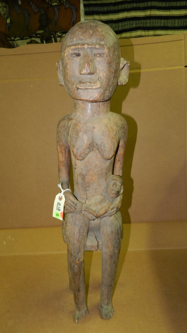 219) African carved Nyamwezi style female figure, seate: 219) African carved Nyamwezi style female figure, seated on a stool, infant held across lap, wood w/brown stain, soiled. From Tanzania. G COND for age. Cracks on front & arm, repaired break to stool a