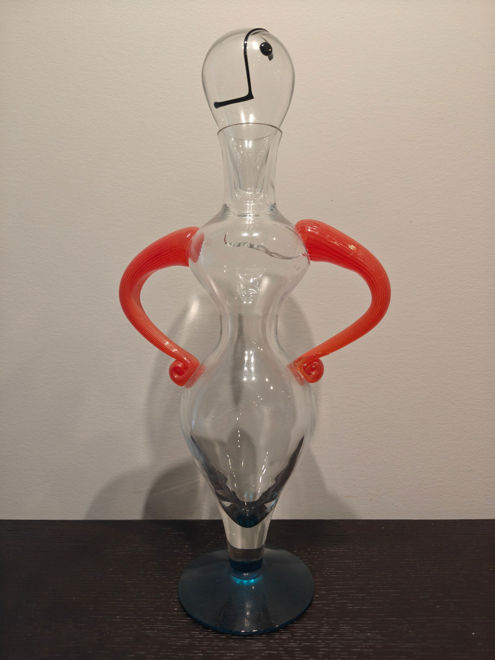Kosta Boda Kjell Engman "Fenix" Lady Decanter: Kosta Boda art glass decanter designed by Kjell Engman, part of the "Fenix" series. Clear glass form with bold sculptural red handles, blue base, and stylized face decoration on the removable stopper.