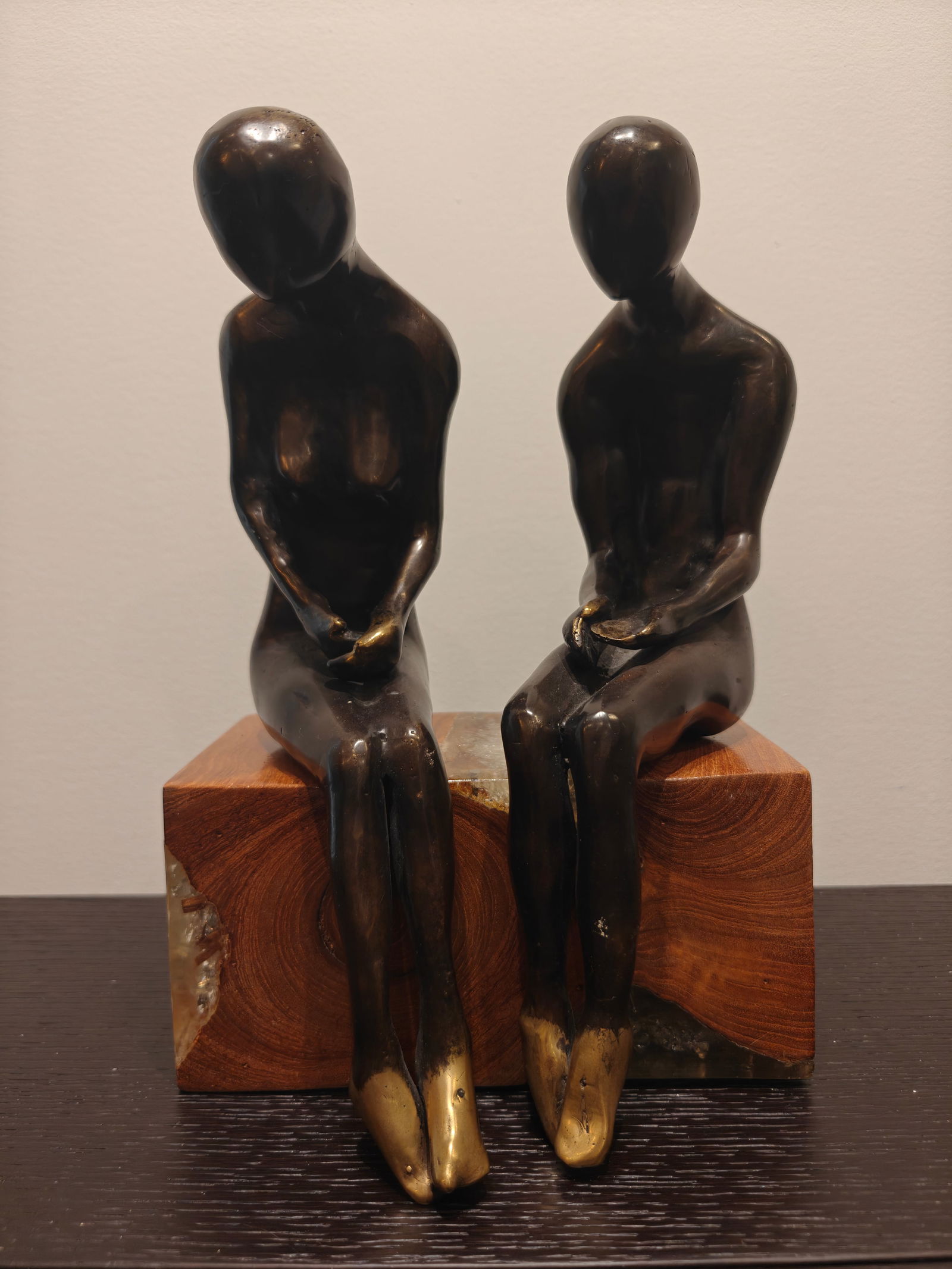 Bronze “Sitting Couple” Sculpture on Wood and Glass Base: Modernist bronze sculpture depicting a stylized seated couple, male and female, rendered with elongated, faceless forms. Both figures are finished in dark patinated bronze with polished highlights at