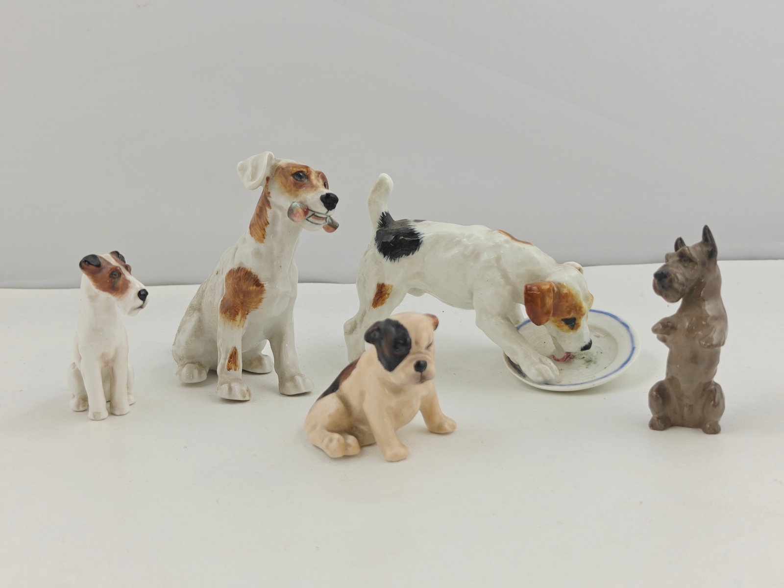 Set of 5 Royal Doulton Porcelain Dog Figurines: Description: A group of five Royal Doulton hand-painted porcelain dog figurines, each modeled in naturalistic poses. The lot includes: a terrier seated with bone in mouth, model HN1157; a seated terri
