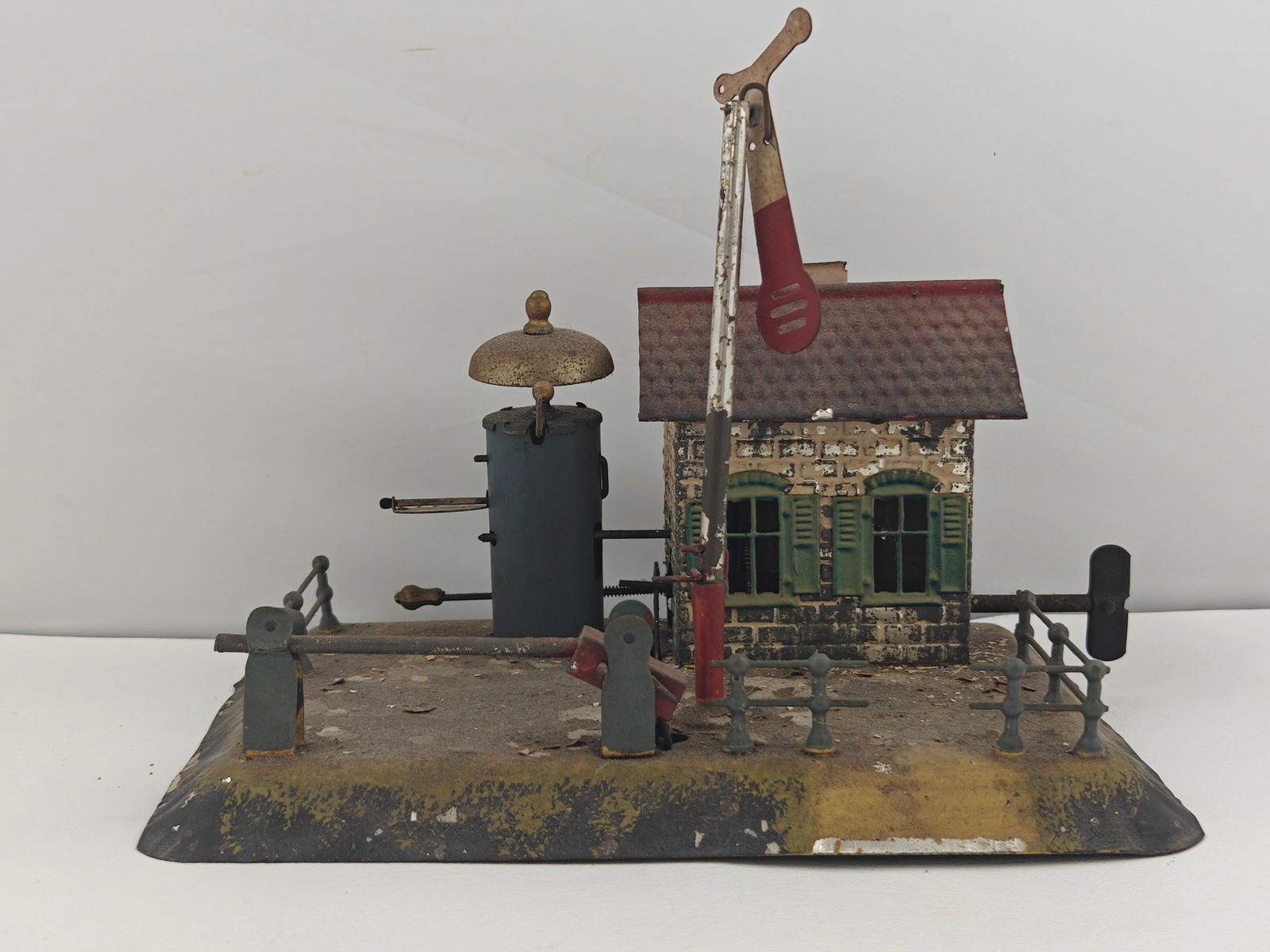 Antique Tin Wind Up Signal House - German Made: German-made tinplate signal house, measuring 9.5"x6.5"x8". Features original lithographed paint with visible chipping and age wear. Includes working signal arm, bell, and fencing detail. Marked "Made