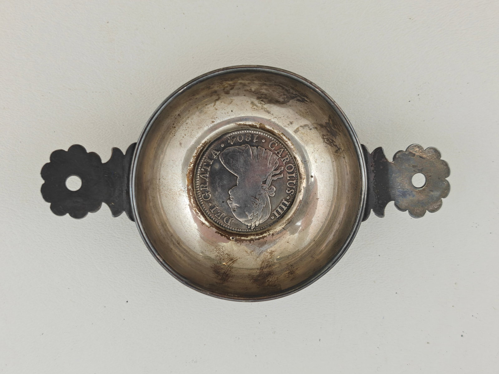 Sterling Silver Tastevin Wine Tasting Bowl with Charles IIII of Spain 1804 Coin: A sterling silver tastevin wine taster featuring a mounted 1804 Spanish Colonial 8 Reales coin of King Charles IIII. One side of the coin shows the crowned coat of arms of Spain flanked by the Pillars