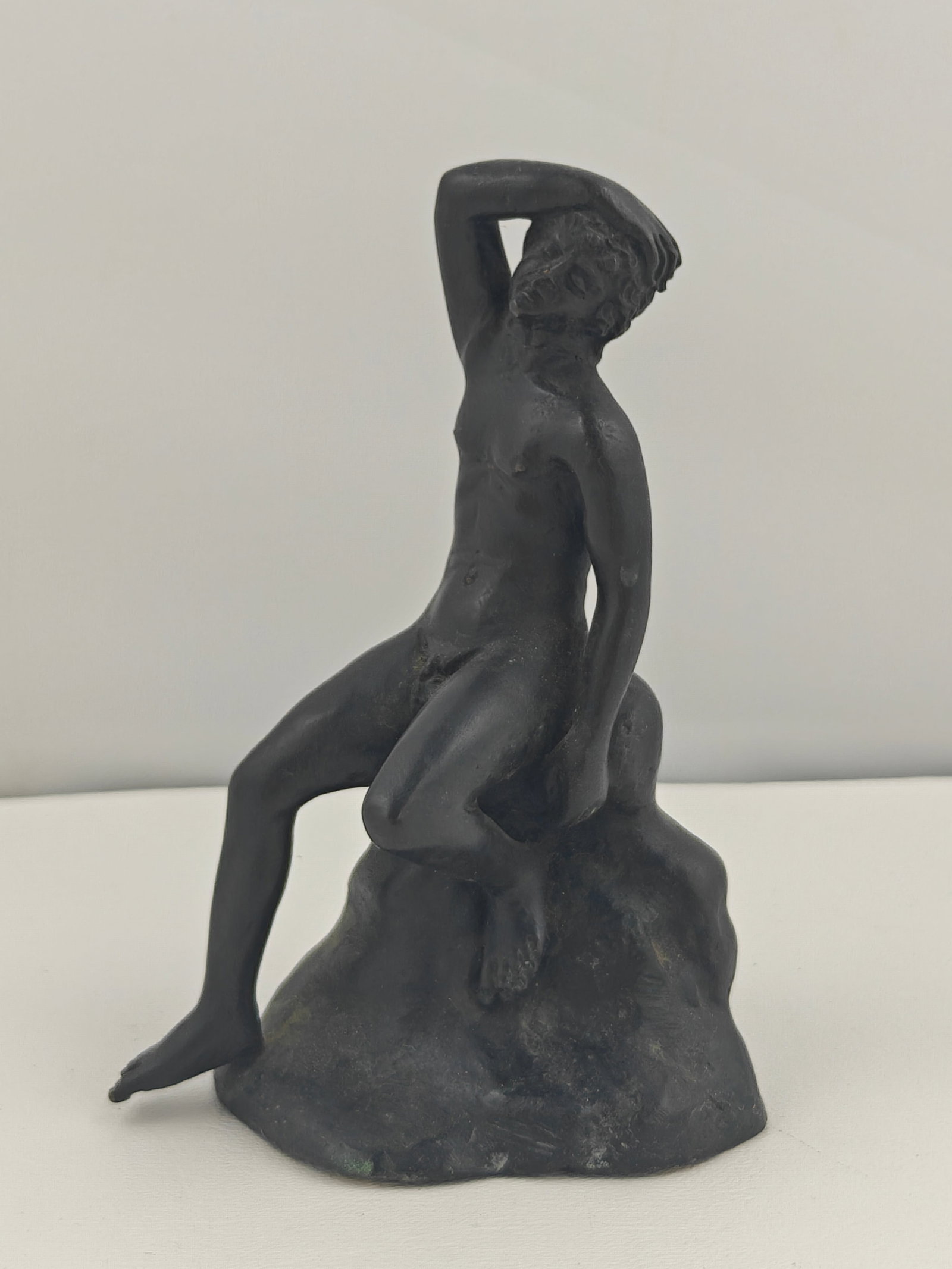 19th Century Bronze Nude Figure on Rock: Small bronze sculpture depicting a seated nude figure, hand resting on head, draped over a naturalistic rock formation. Exhibits a dark patina with areas of verdigris consistent with age. Likely a Gra