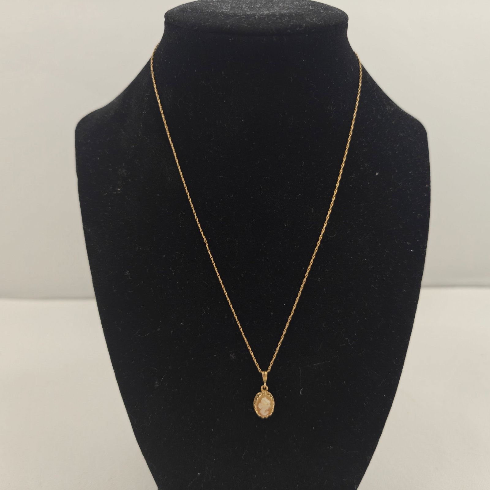 14k Gold Cameo Pendant Necklace: Delicate 14k yellow gold necklace featuring an oval carved shell cameo pendant depicting a classical female profile. The pendant is framed in a decorative gold bezel and suspended from a fine twisted 