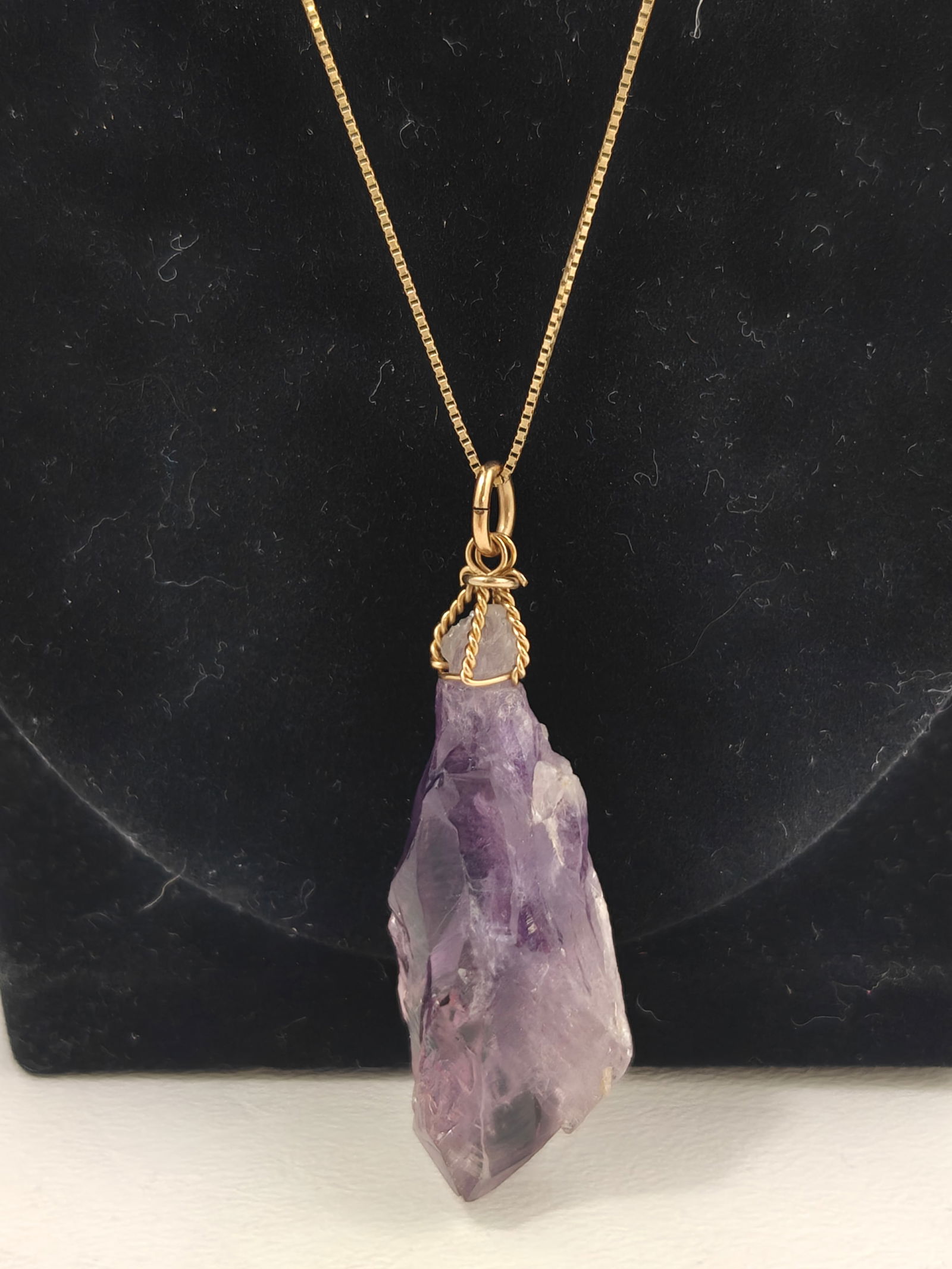Amethyst Pendant on 14K Gold Chain: Natural raw amethyst crystal pendant suspended from a fine 14K yellow gold chain marked "14KT Italy." The pendant features a wire-wrapped gold bail design highlighting the stone's organic form and ric