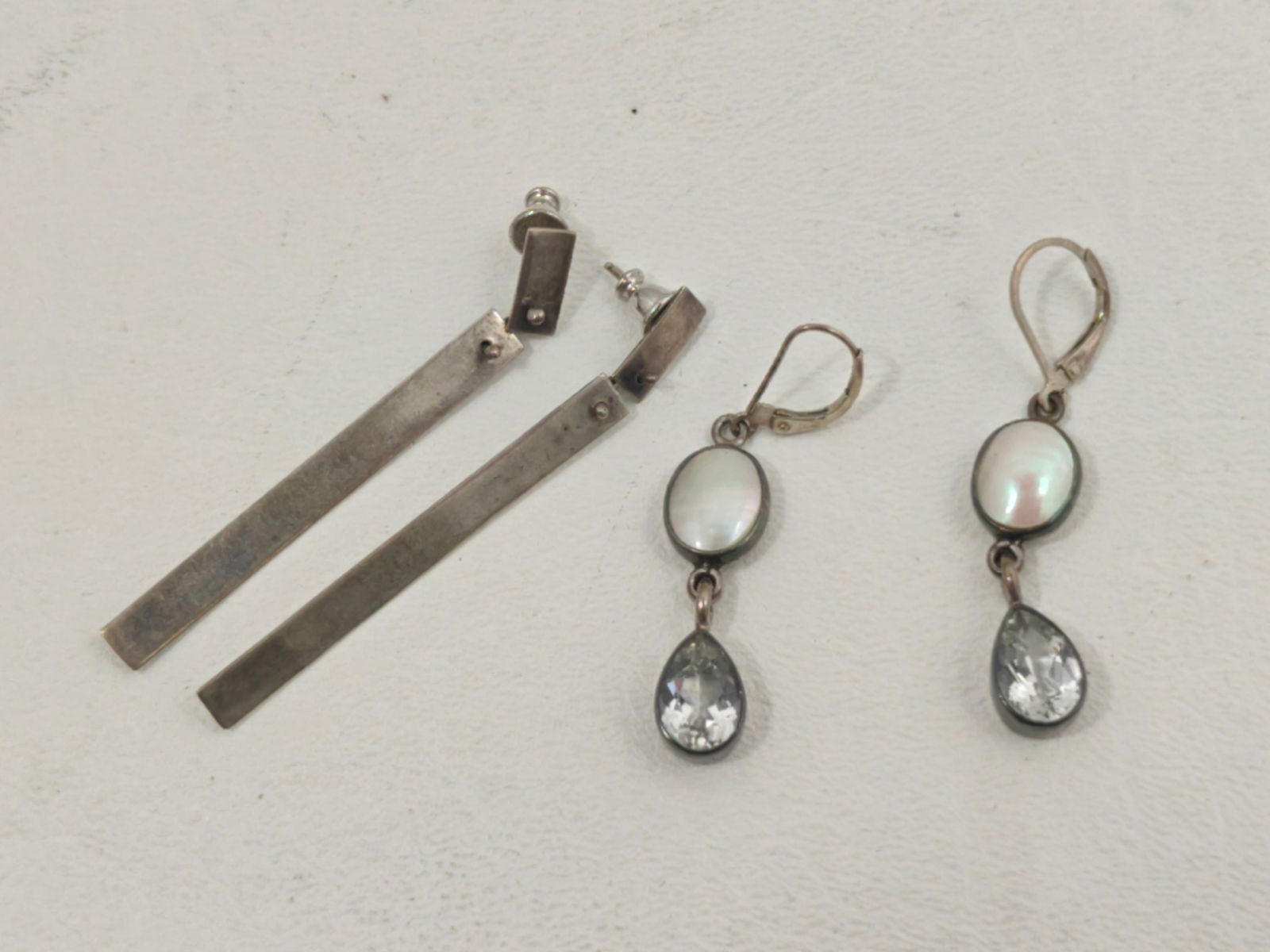 2 Pair Sterling Pierced Earrings: Two pairs of sterling silver pierced earrings. One pair features long rectangular bar drop earrings with post backs. The second pair features oval mother-of-pearl drops with faceted teardrop crystal
