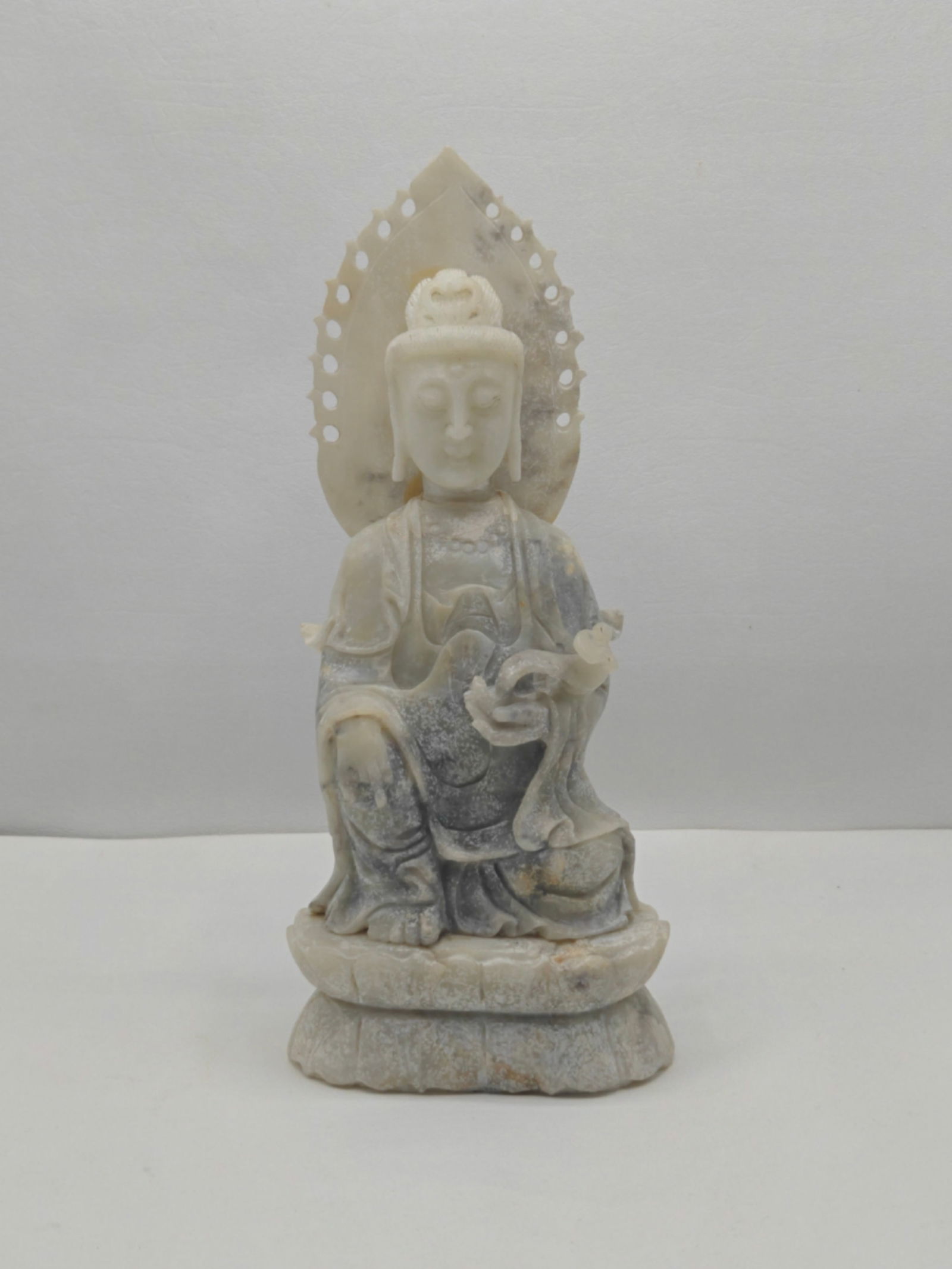 Carved Soapstone Figure of Guanyin Seated on Lotus Base: Finely carved stone sculpture, likely soapstone, depicting Guanyin, the Bodhisattva of Compassion, seated in a relaxed pose on a lotus-form base. The figure is shown with a serene expression and detai